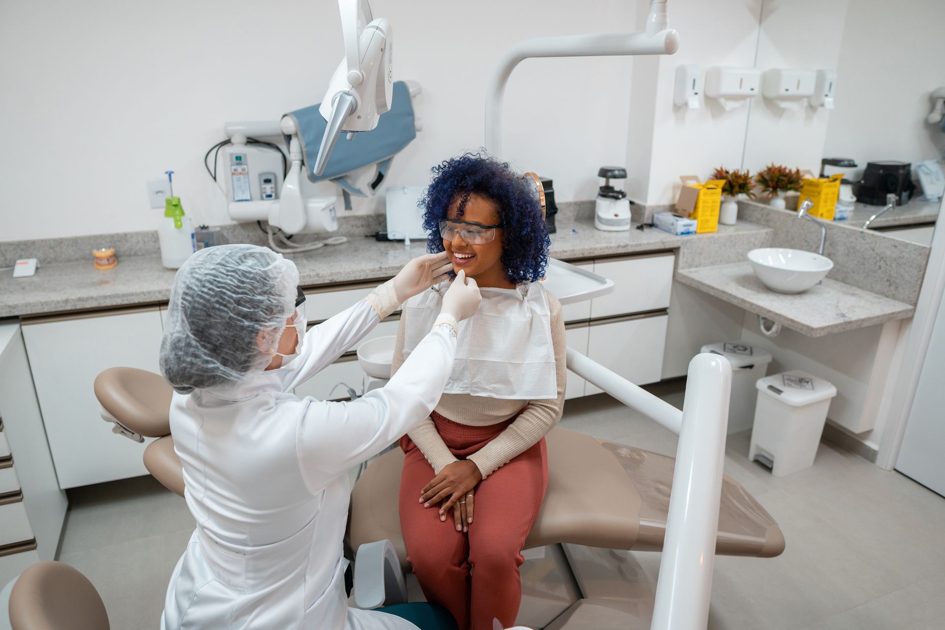 A woman sits in a dental chair during a general dentistry exam while the dentist checks her teeth.
