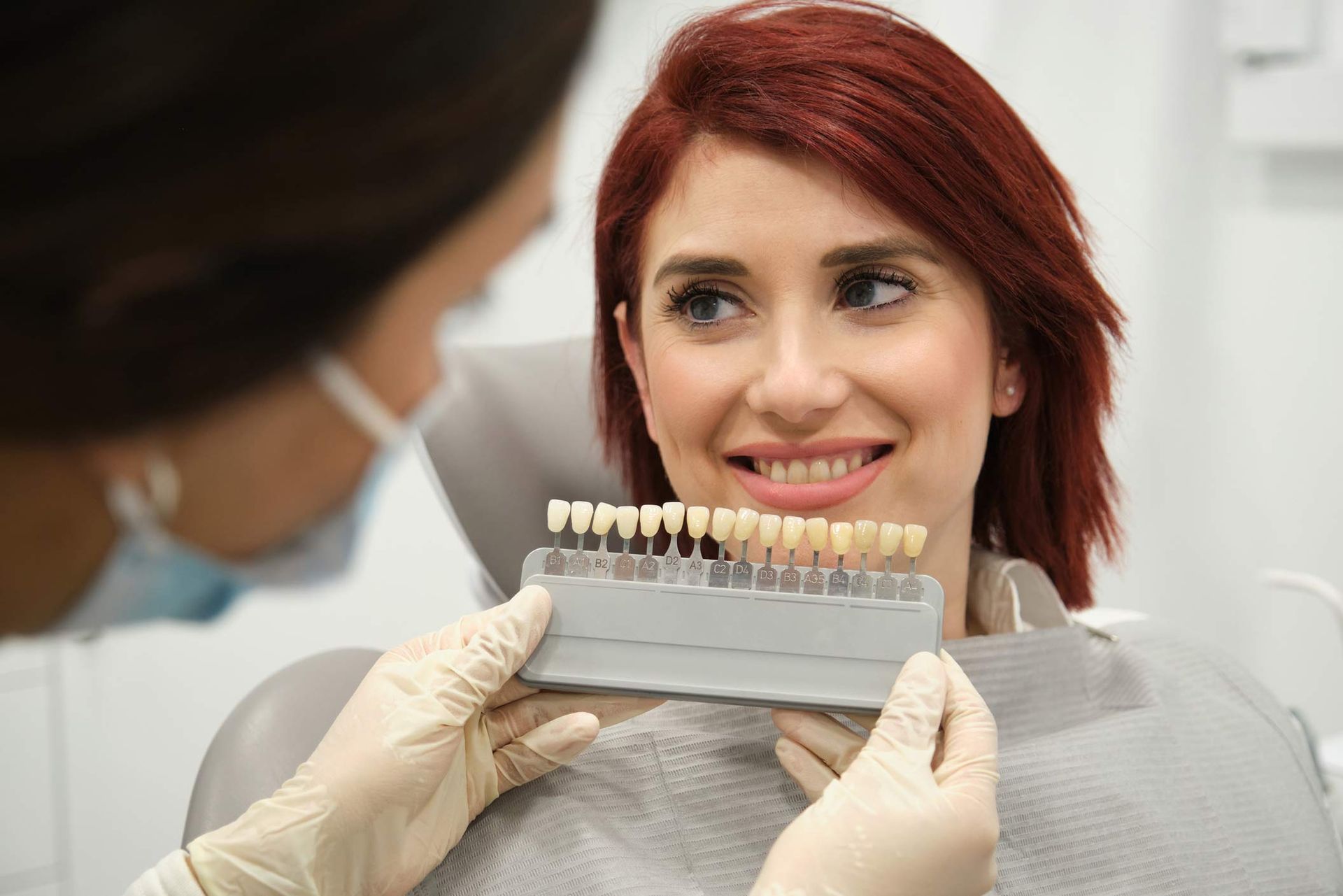 A dentist is comparing a patient’s teeth color with samples for whitening. A dentist is comparing a patient’s teeth color with samples for whitening.
