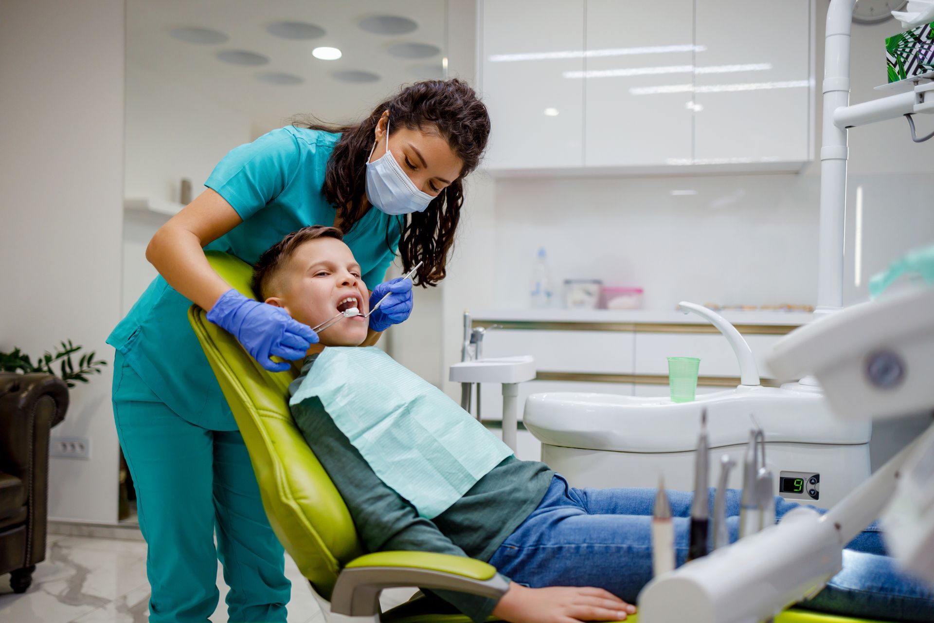 A young boy is sitting in a dental chair while a dentist examines his teeth.