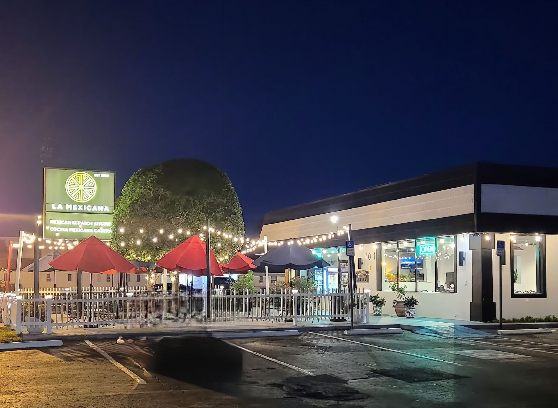 A restaurant with tables and umbrellas in front of it at night.