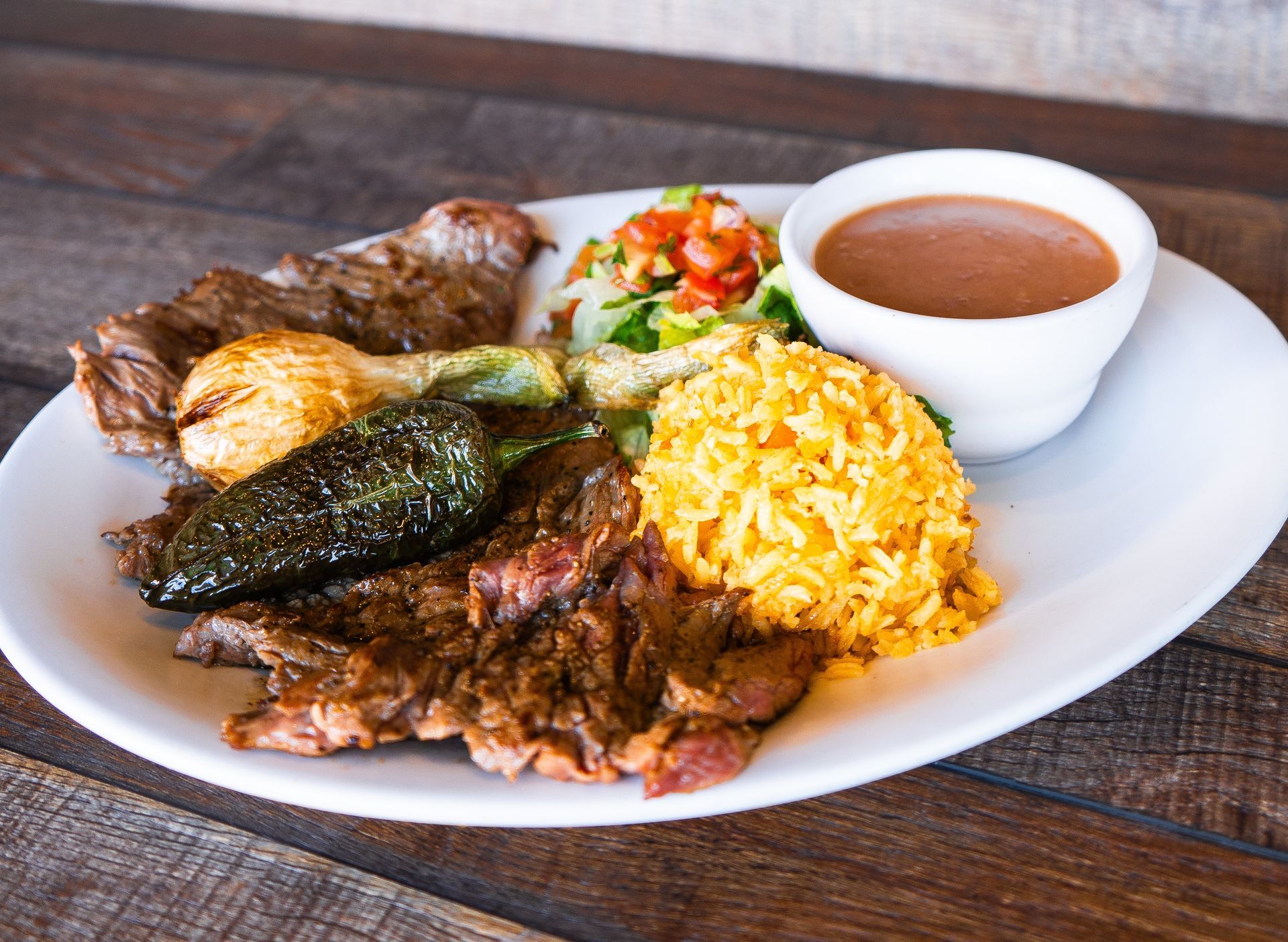 A plate of food with rice , meat and vegetables on a wooden table.