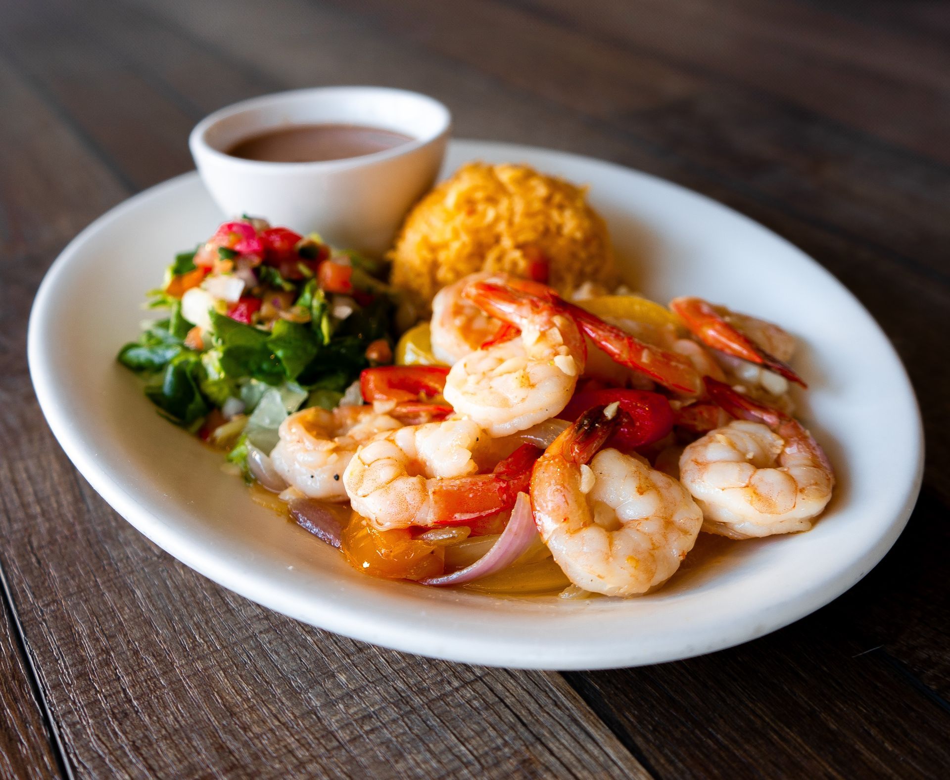 A white plate topped with shrimp and rice on a wooden table