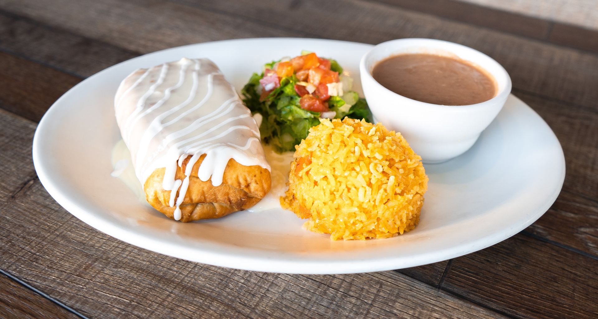 A white plate topped with a burrito , rice and beans.