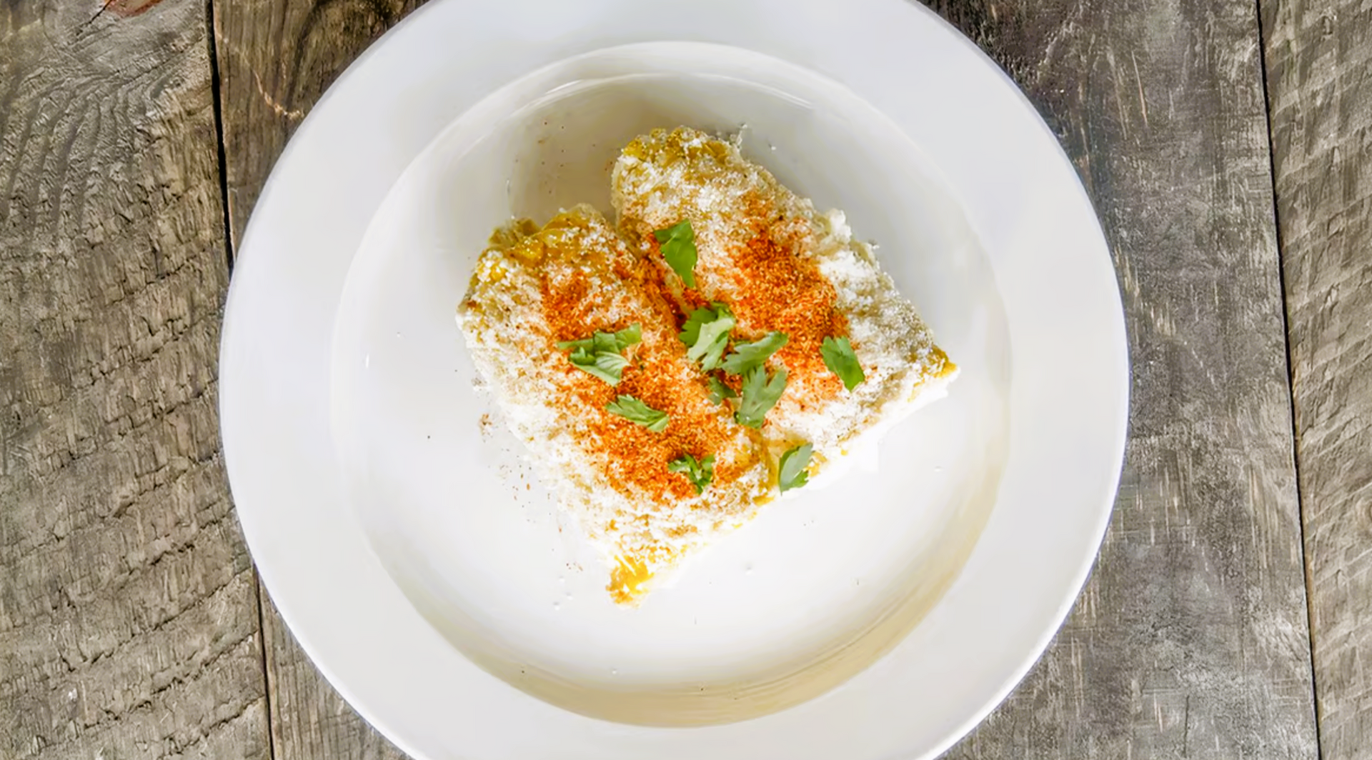 A white plate topped with corn on the cob on a wooden table.