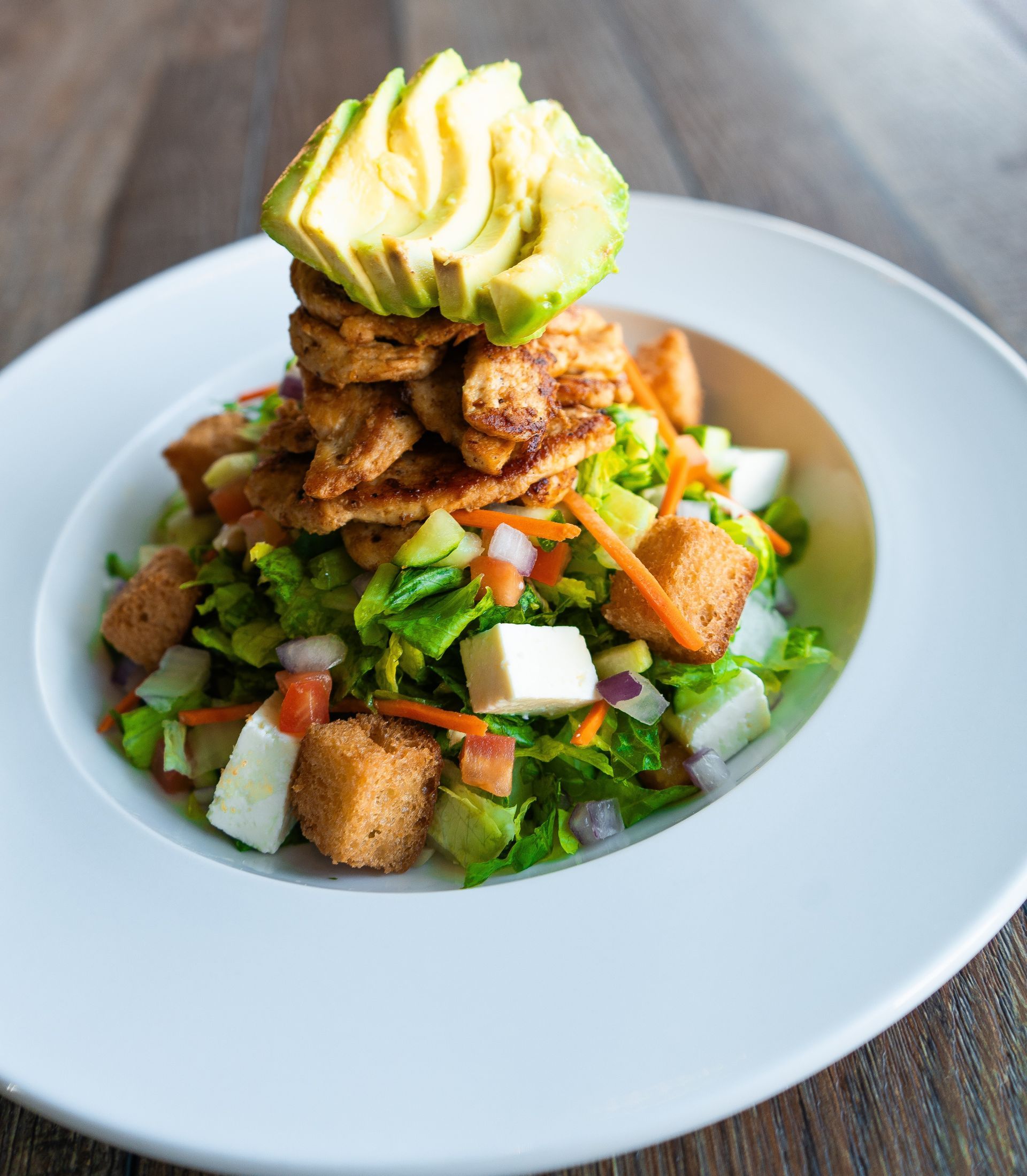 A white plate topped with a salad and avocado on top.