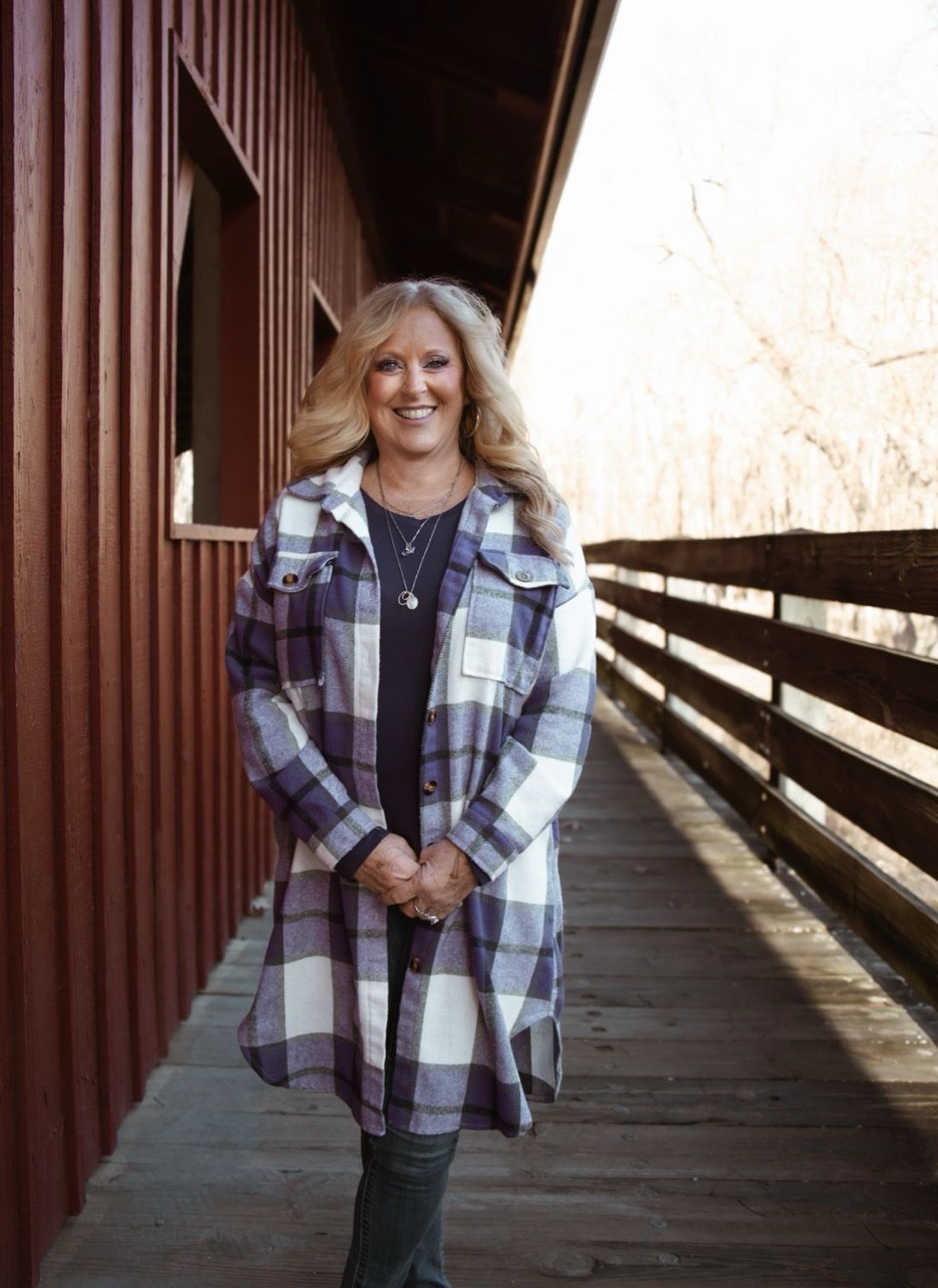Woman in plaid shirt and jeans stands on wooden bridge with red side.