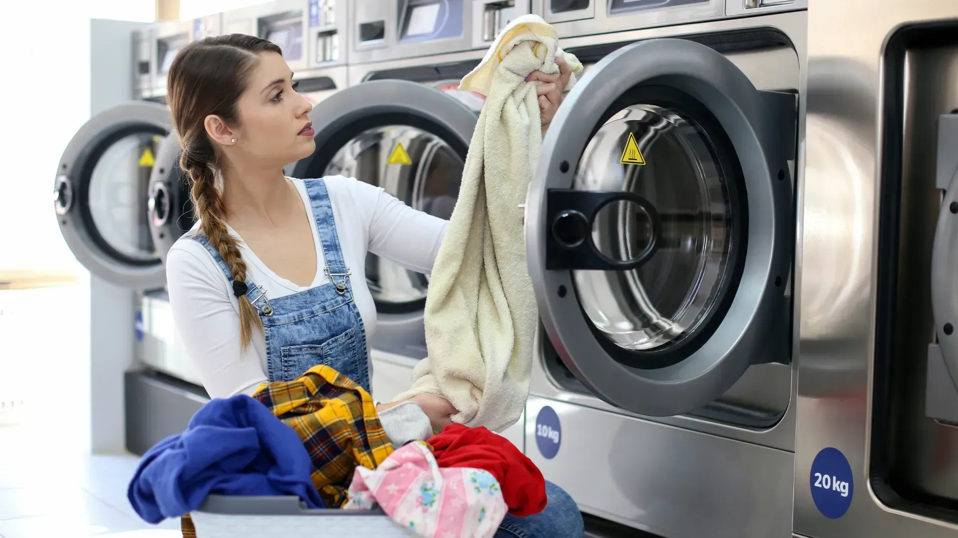 Woman loading clothes into a washing machine at a laundromat.