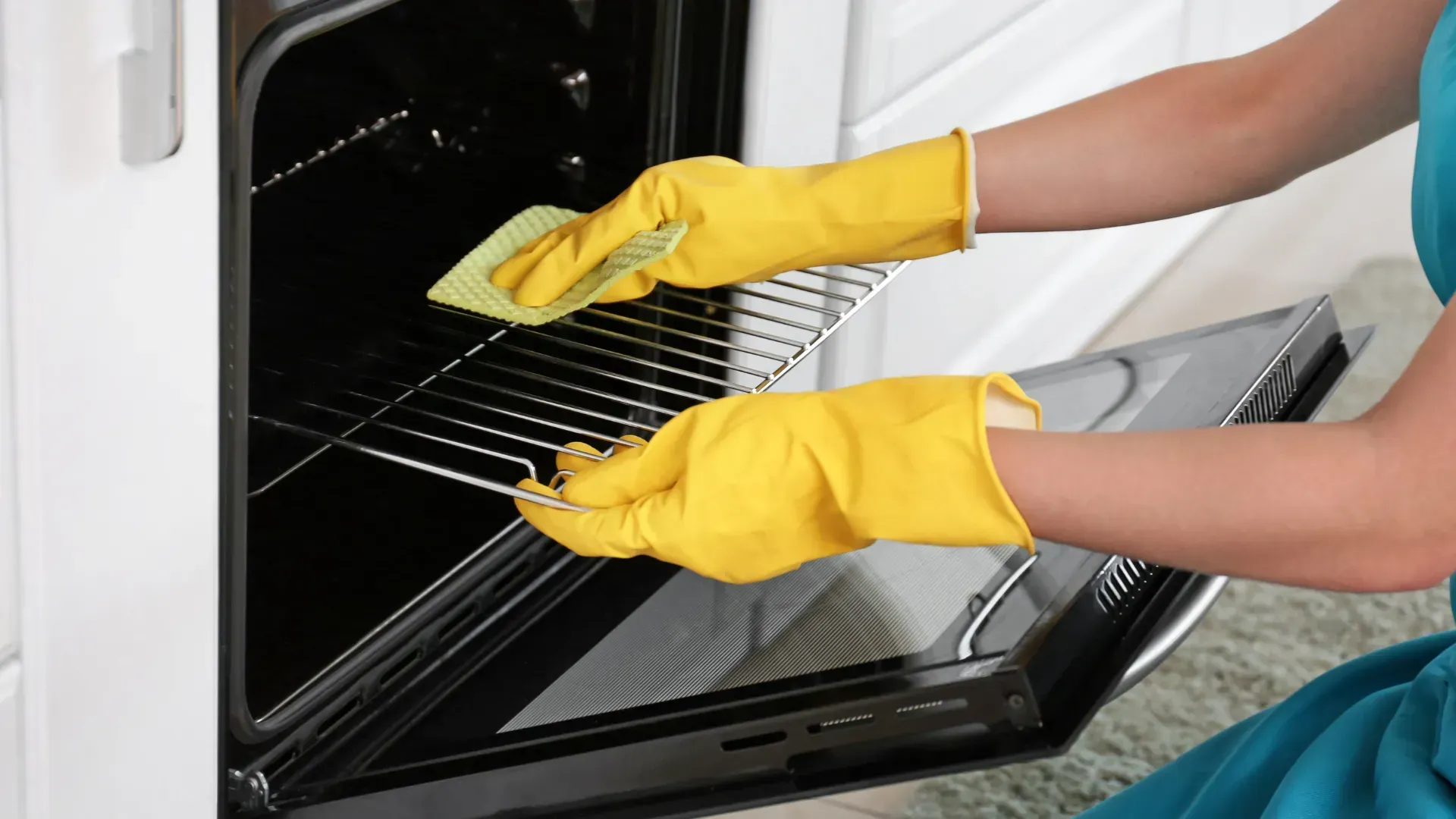 Person wearing yellow gloves cleaning an oven, wiping the interior with a cloth.