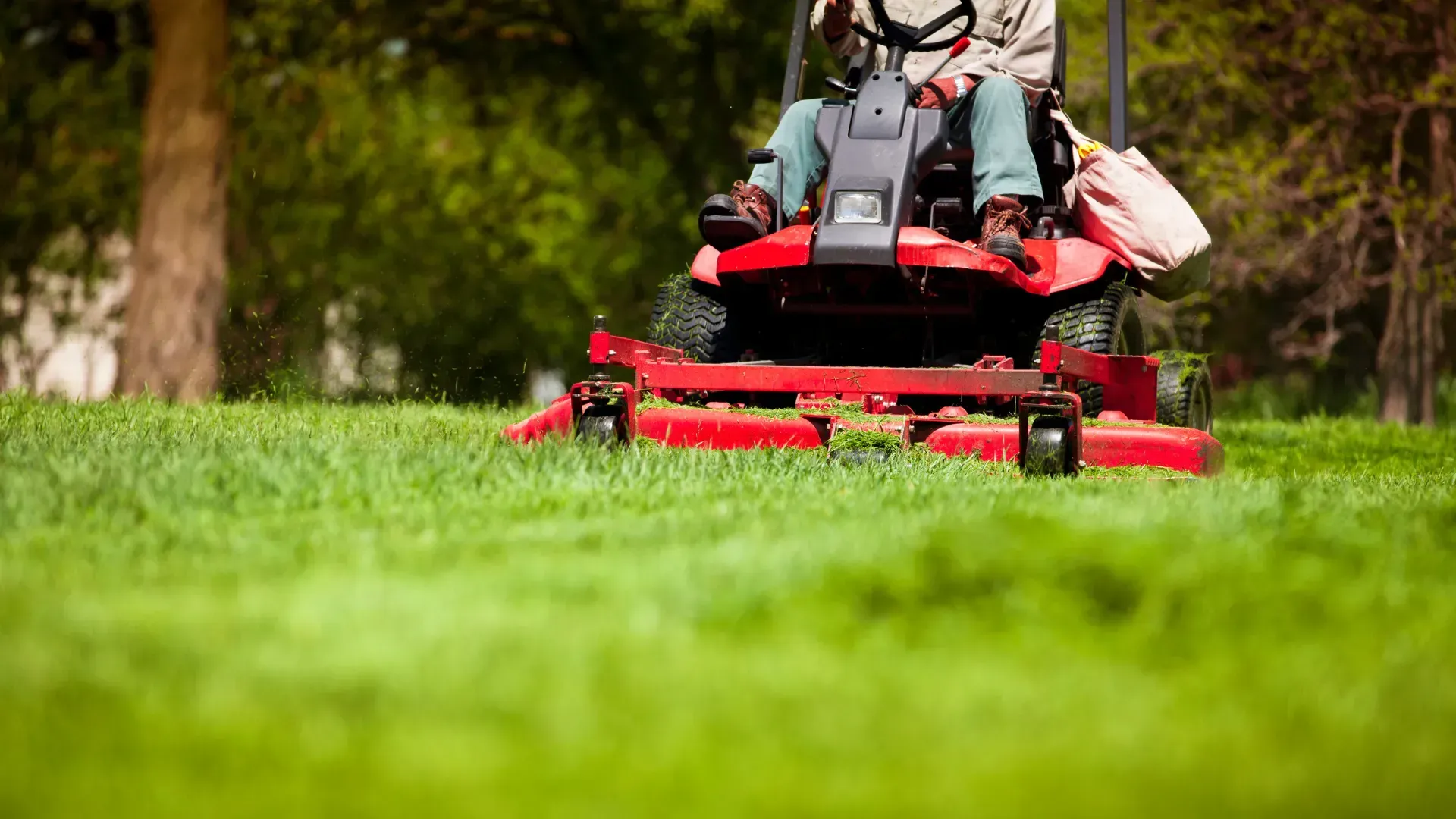 Red riding lawn mower mowing a green lawn in a park.