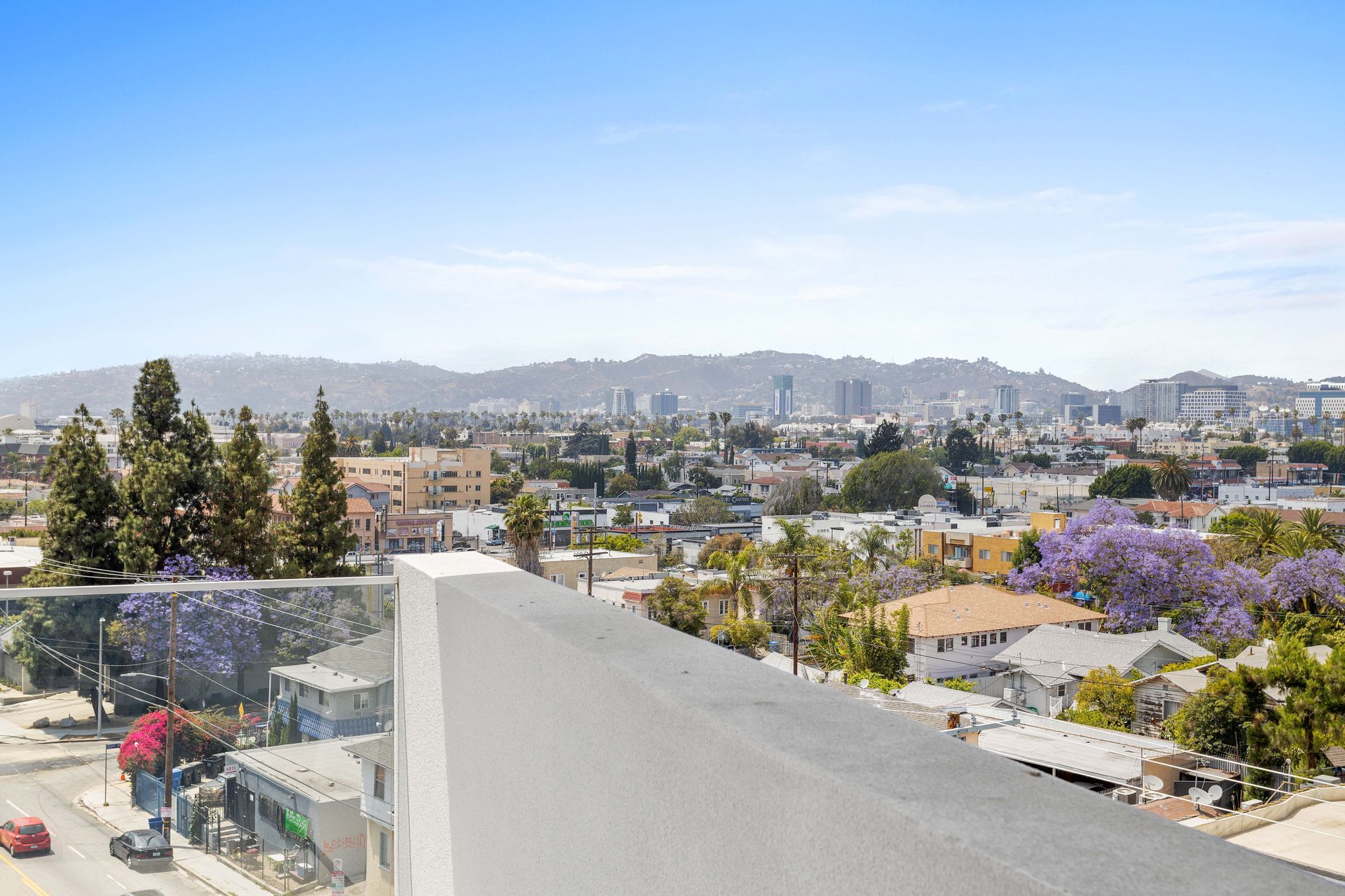 View of a city skyline from a rooftop with trees and a clear blue sky.