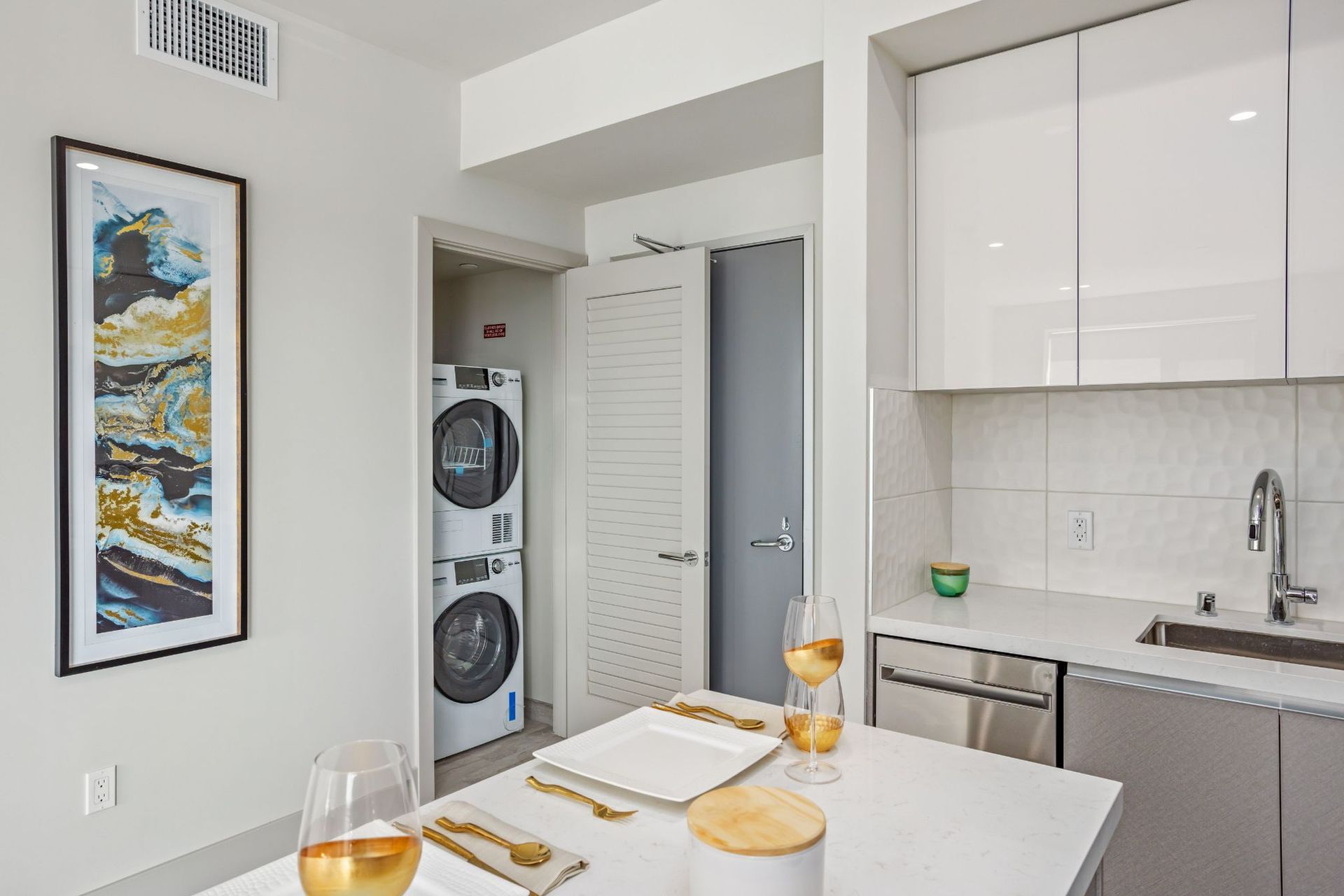 Modern kitchen with stacked washer/dryer, white cabinets, island with place settings, art print.