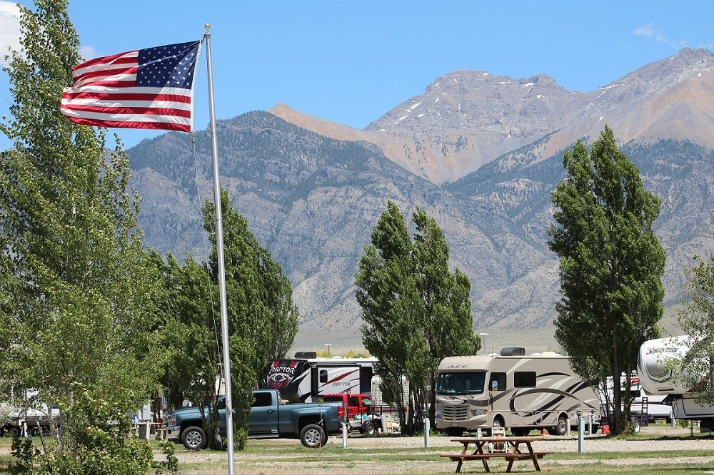 An american flag is flying in front of a campground with mountains in the background.