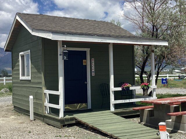 A small green shed with a porch and a picnic table.