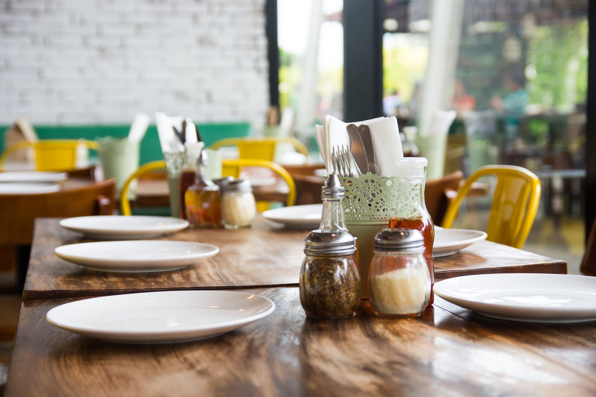 A restaurant with plates and condiments on the tables.