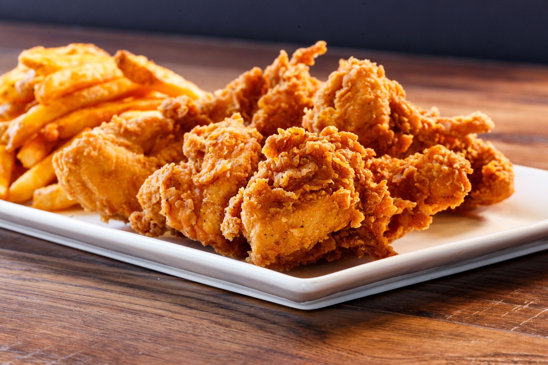 A white plate topped with fried chicken and french fries on a wooden table.