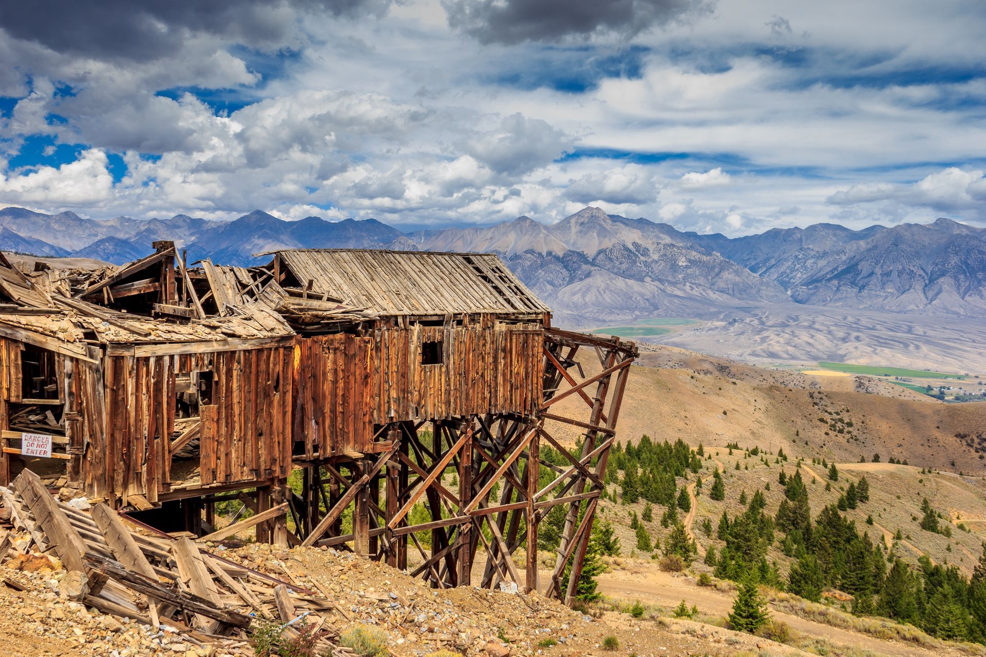 An old wooden building is sitting on top of a hill with mountains in the background.