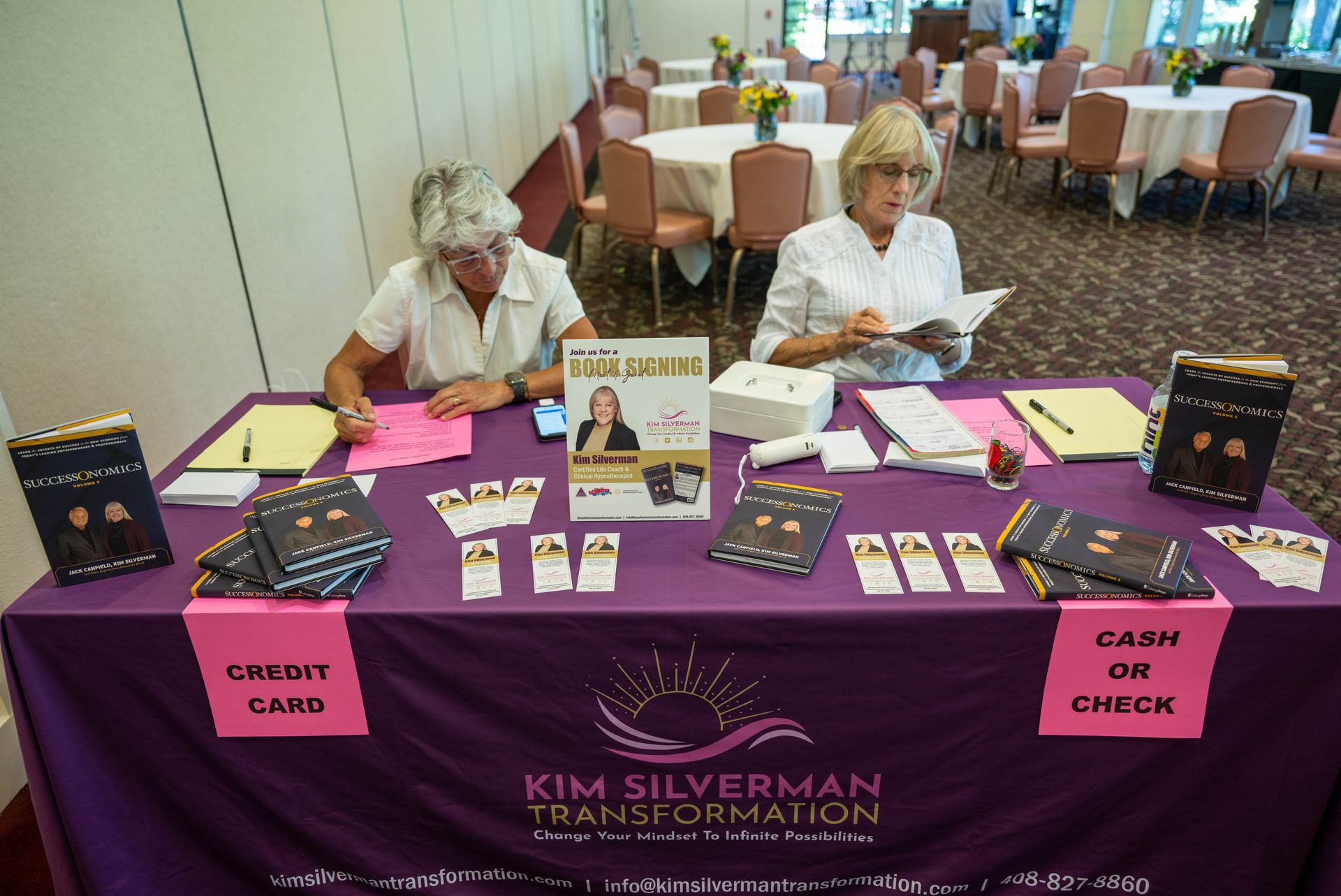 Two women are sitting at a table with a sign that says cash or check.