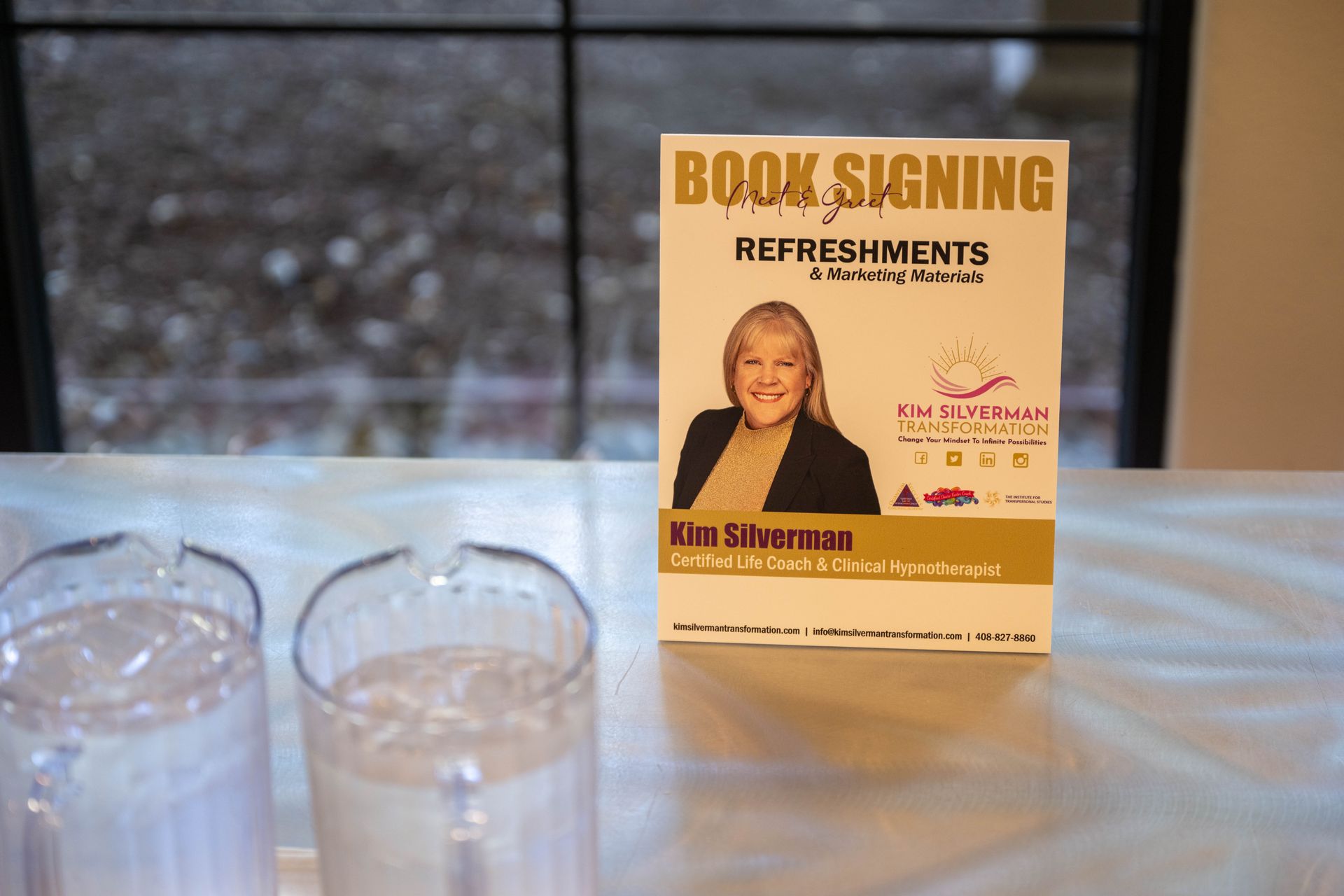 A book signing sign is sitting on a table next to two glasses of water.