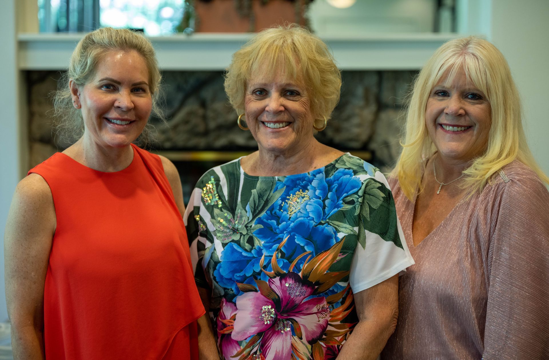 Three women are posing for a picture in front of a fireplace.