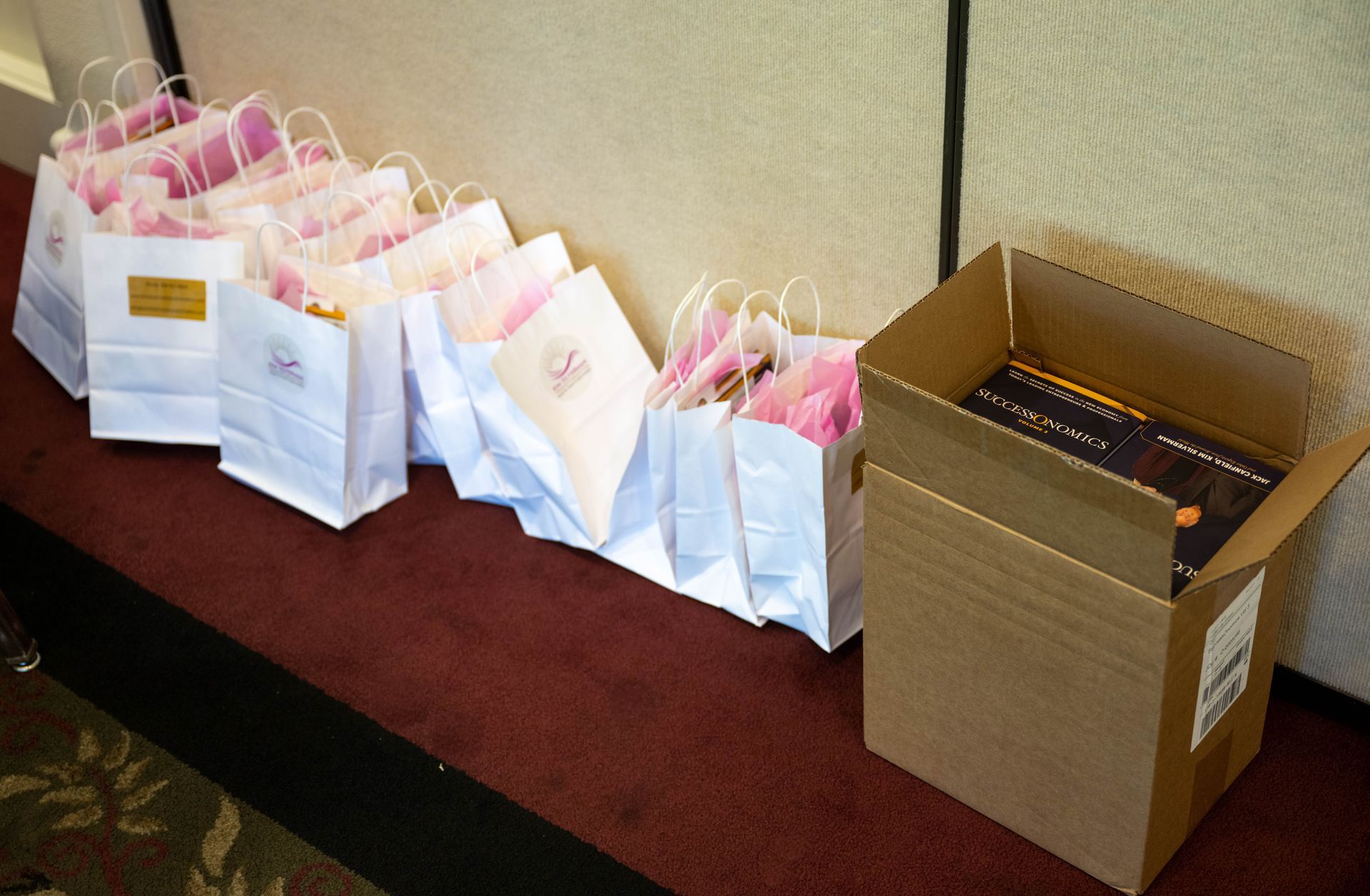 A row of pink and white bags are lined up next to a cardboard box