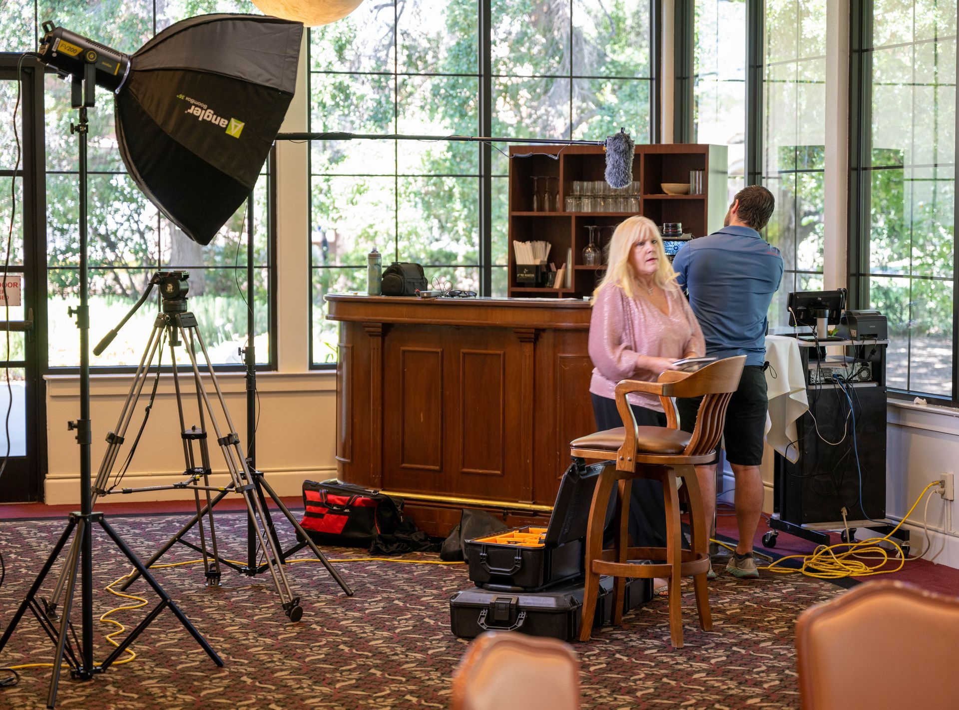 A man and Kim Silverman are setting up equipment in front of a camera in front of a bar.