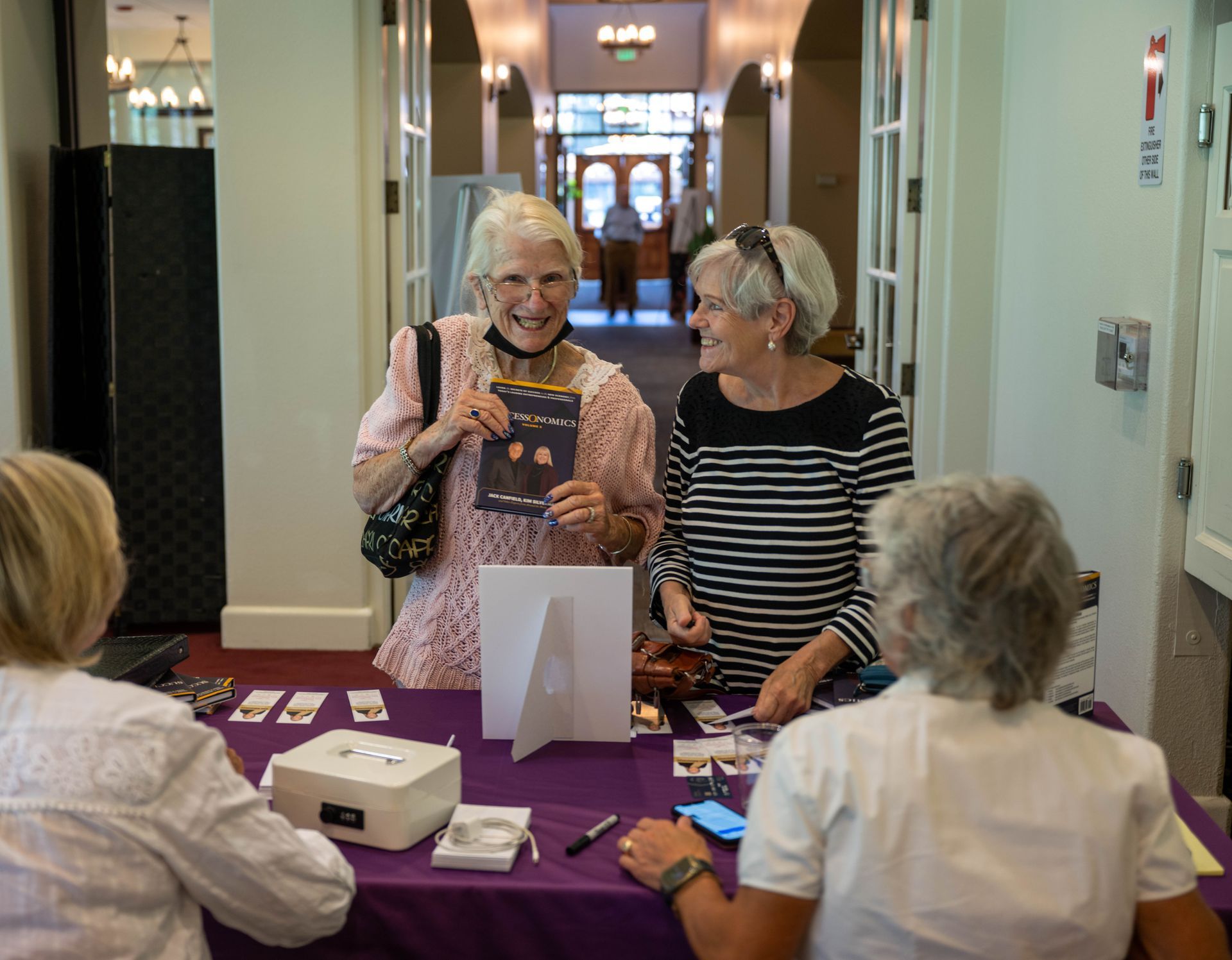 A group of women are sitting and standing at a table talking to each other.