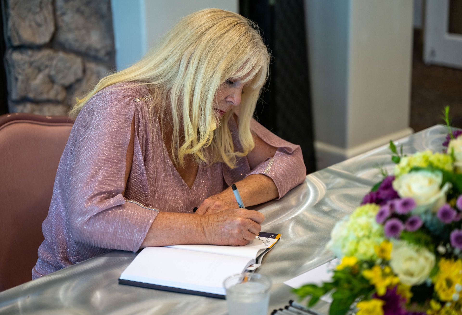 Kim Silverman is sitting at a table writing in a notebook.