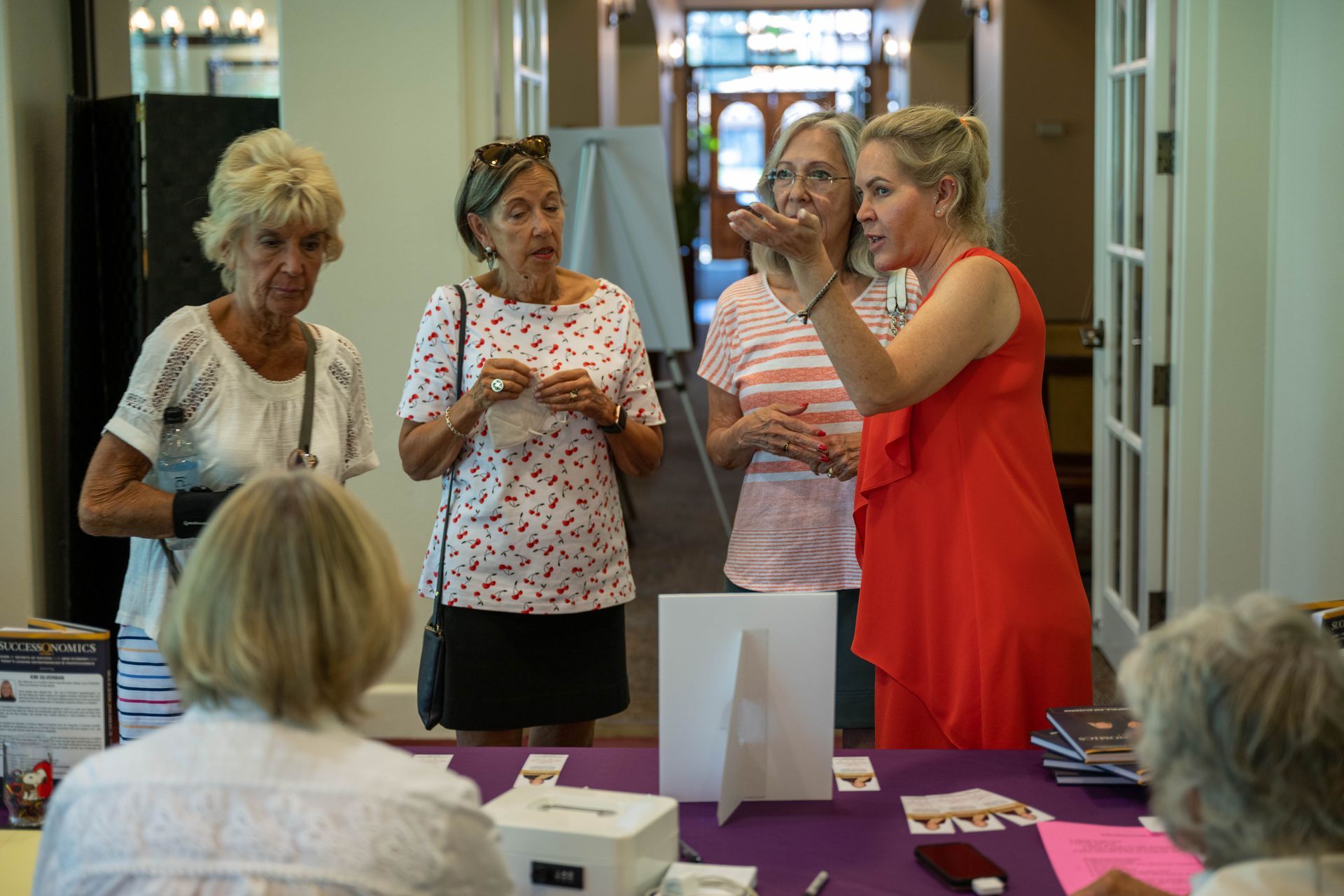 A group of women are standing around a table talking to each other.