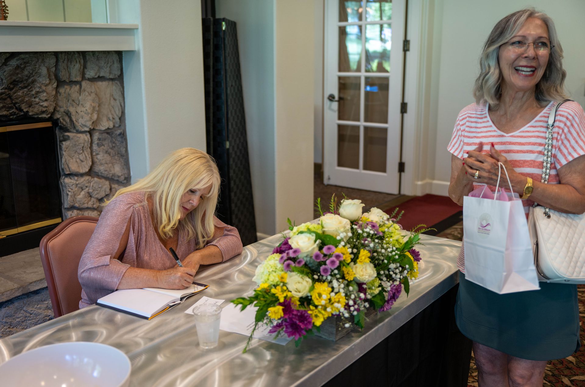 Two women are sitting at a table with flowers on it.