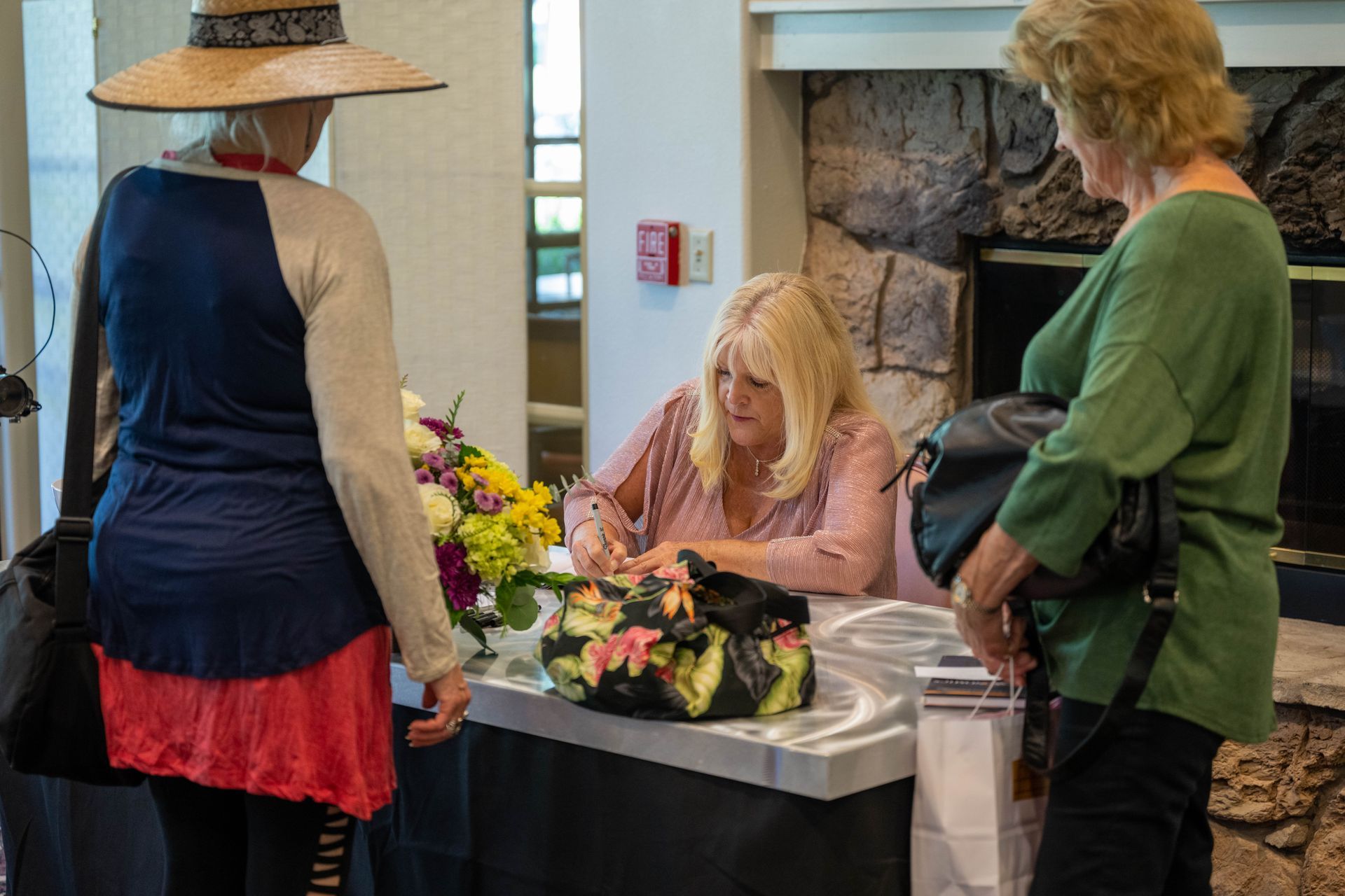 Kim Silverman is signing a book at a table while two other women look on.