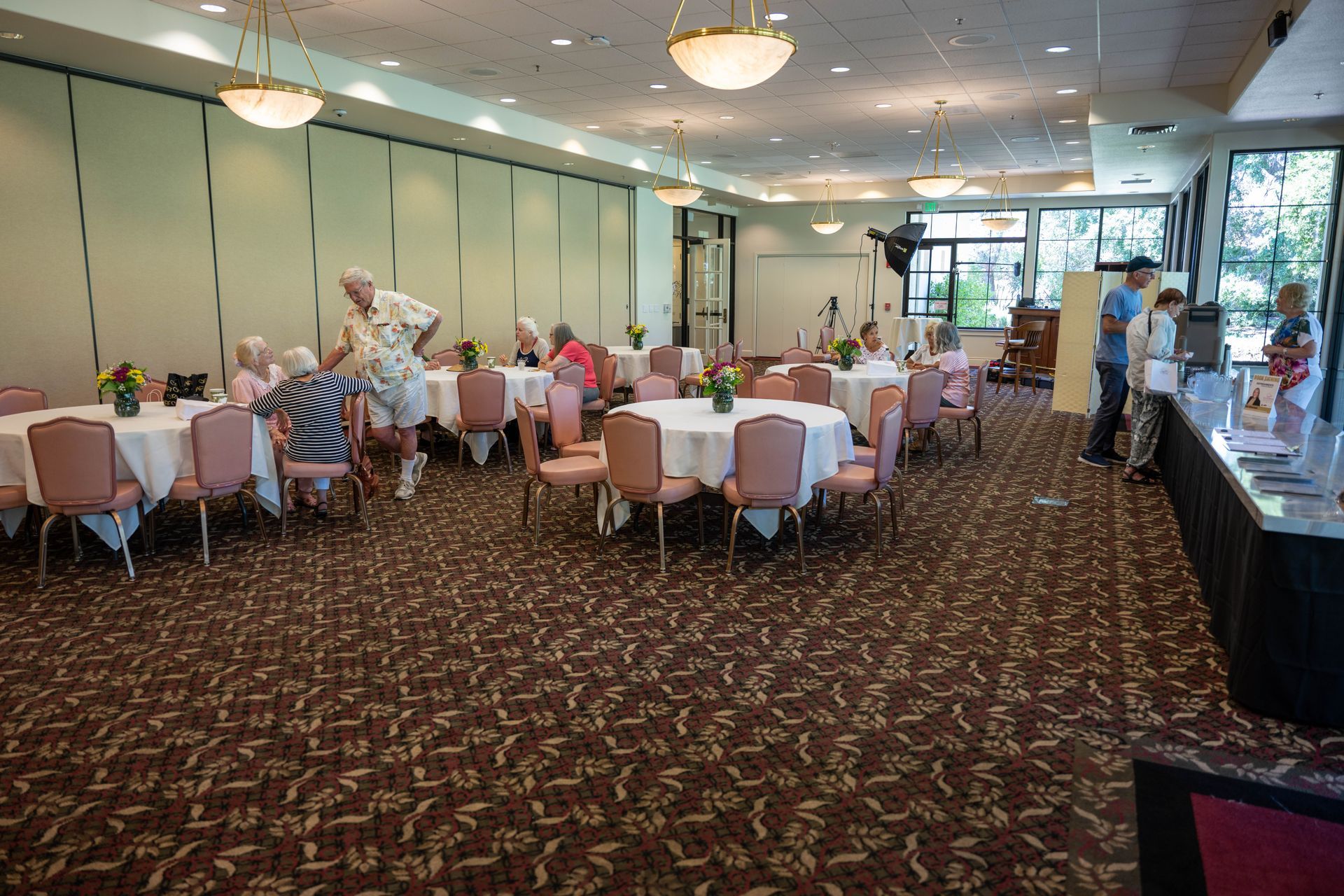 A large room filled with tables and chairs and people standing around.