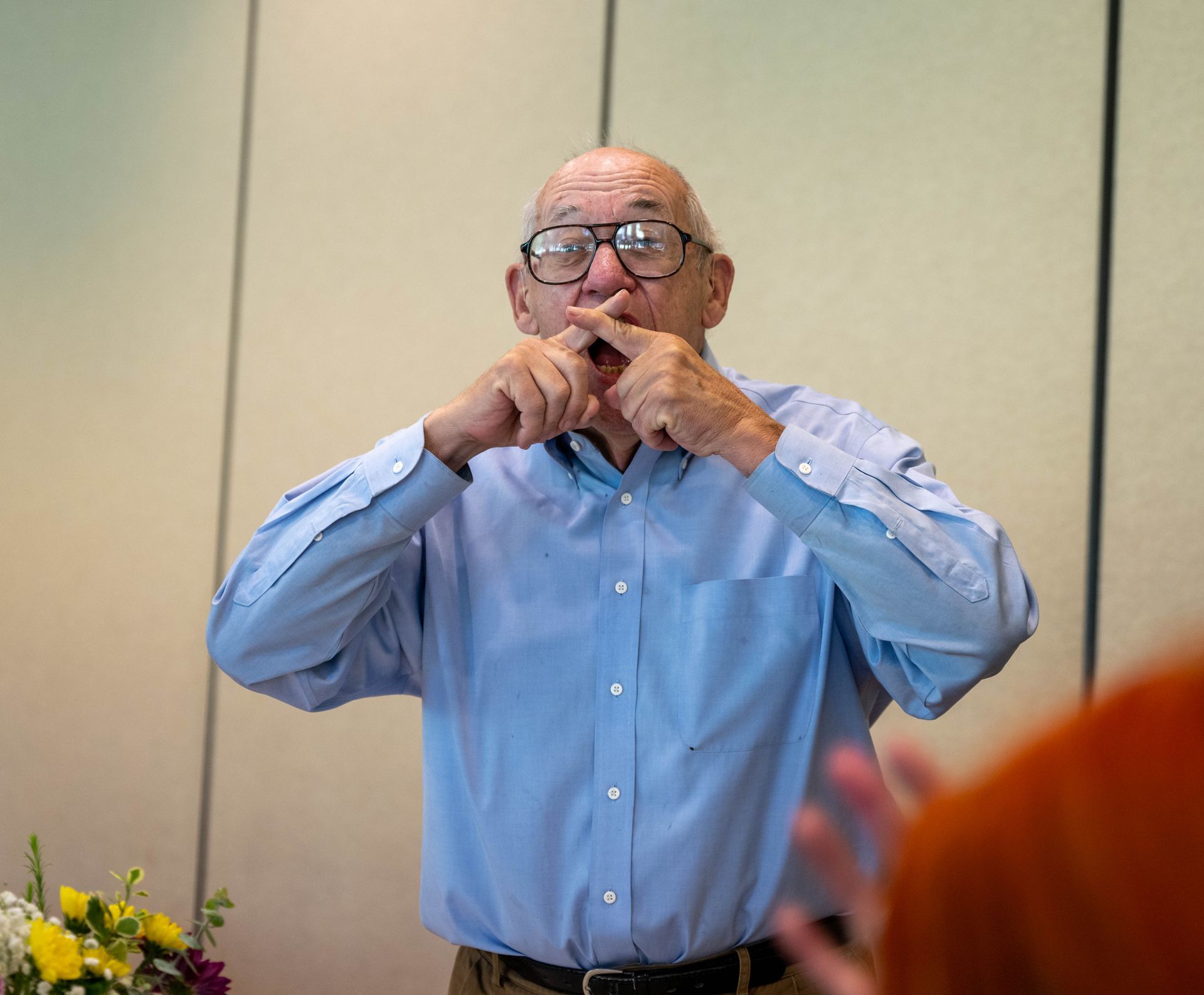 A man wearing glasses and a blue shirt is crossing his fingers in front of his face.