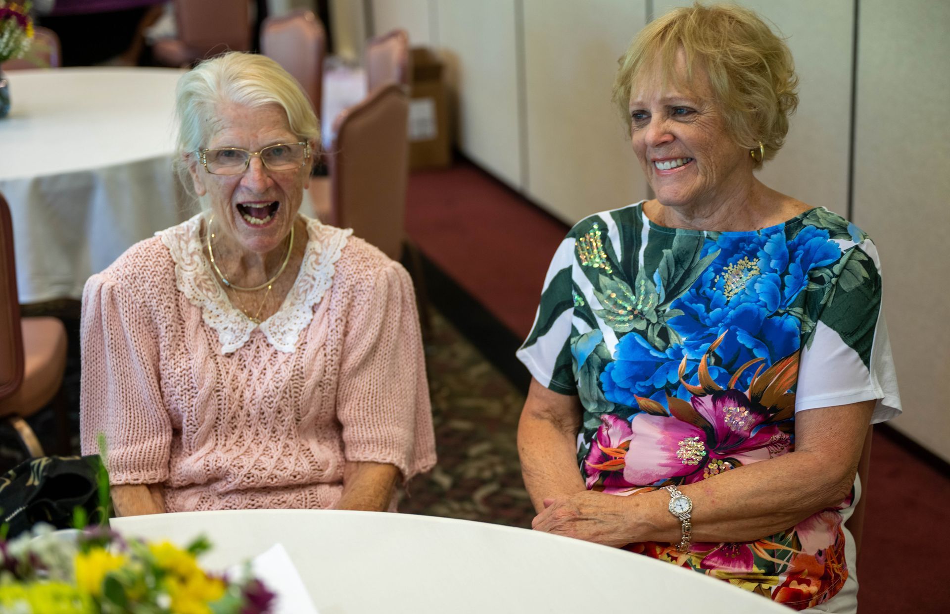 Two older women are sitting at a table laughing.