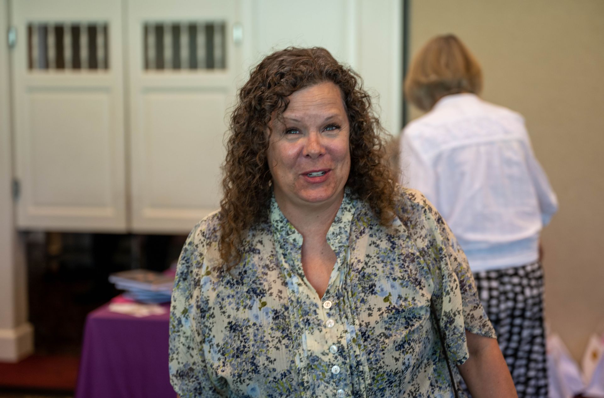 A woman with curly hair is smiling for the camera in a room.