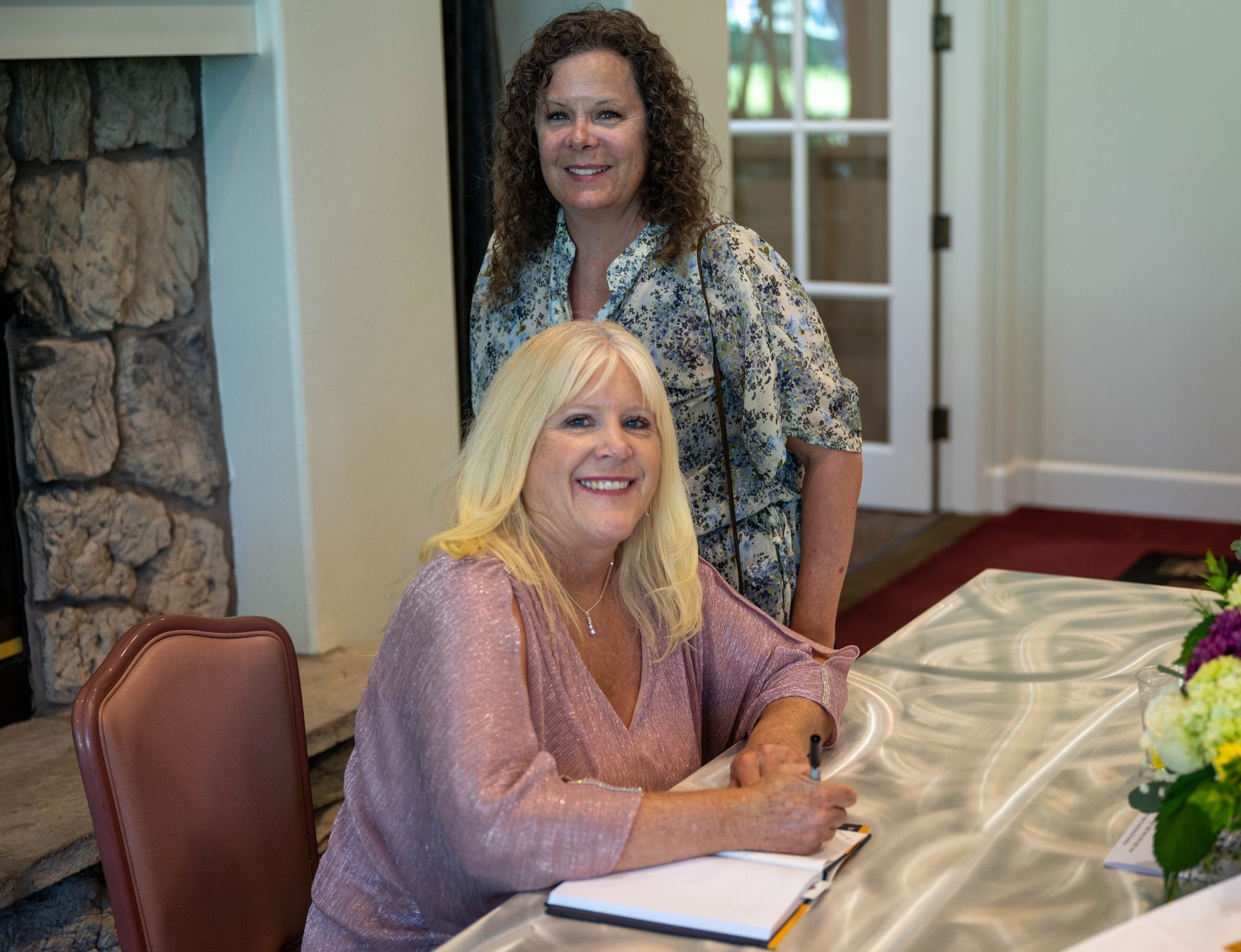 Kim Silverman and a women are sitting at a table signing a book.