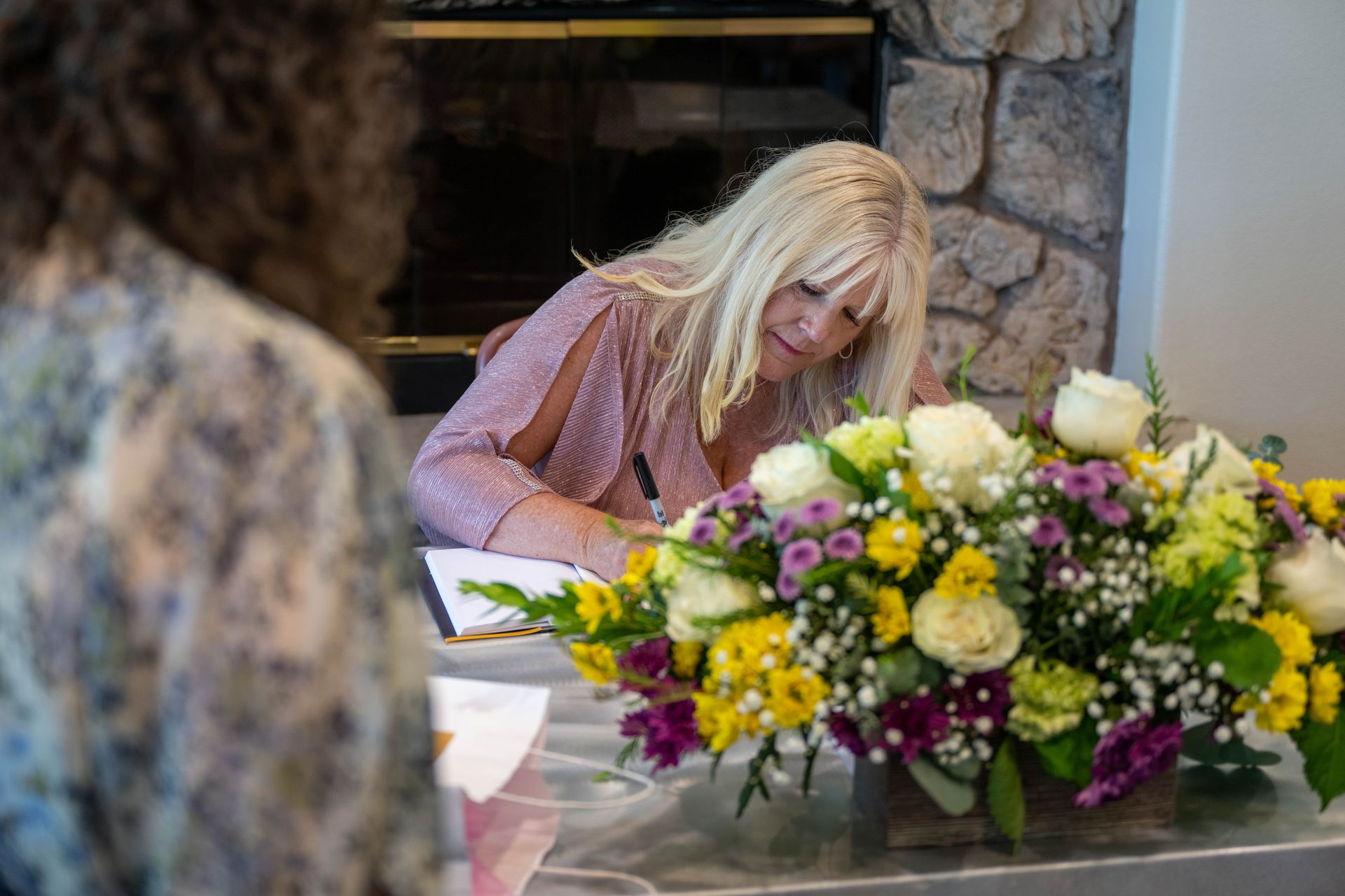 Kim Silverman is writing on book in front of a bouquet of flowers.