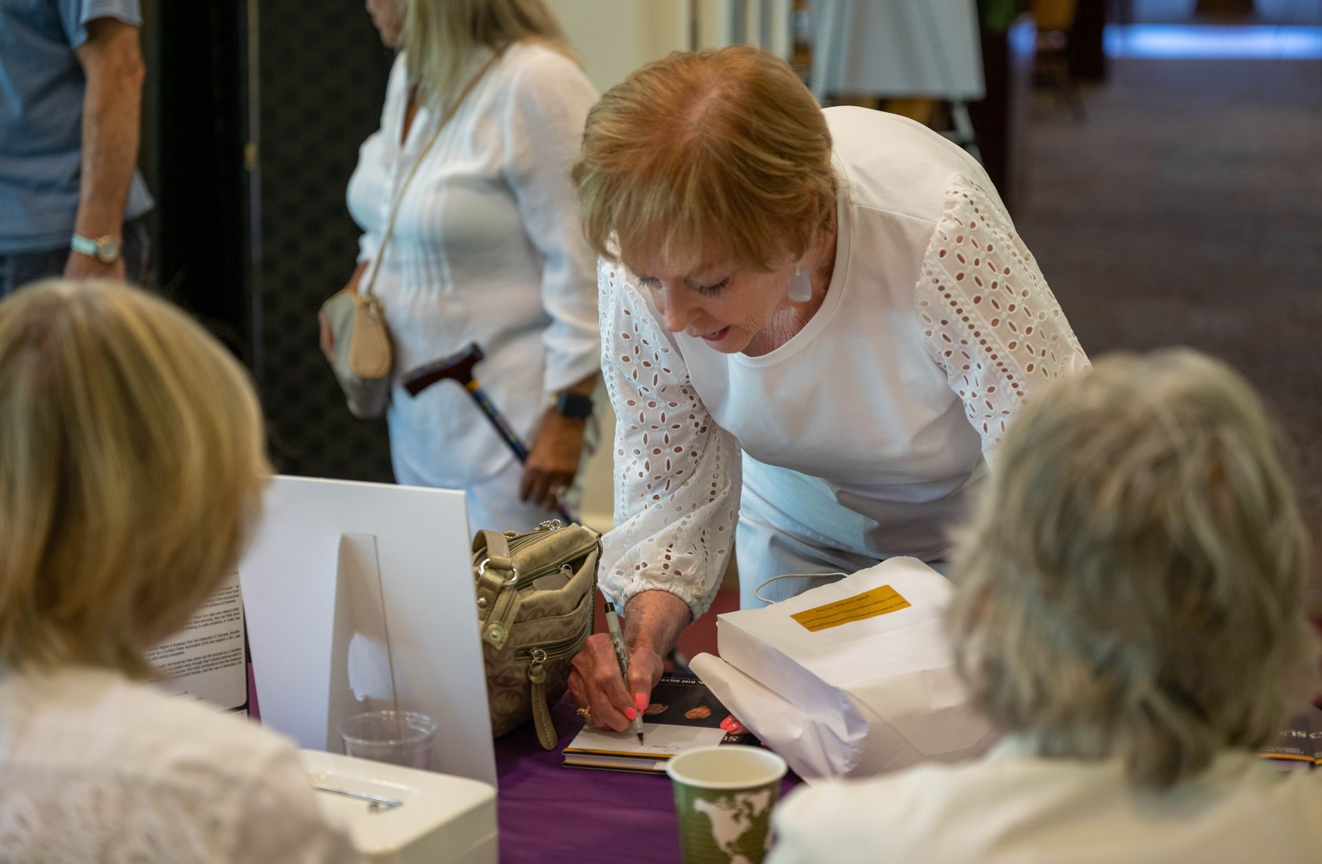 A woman is signing a piece of paper at a table.