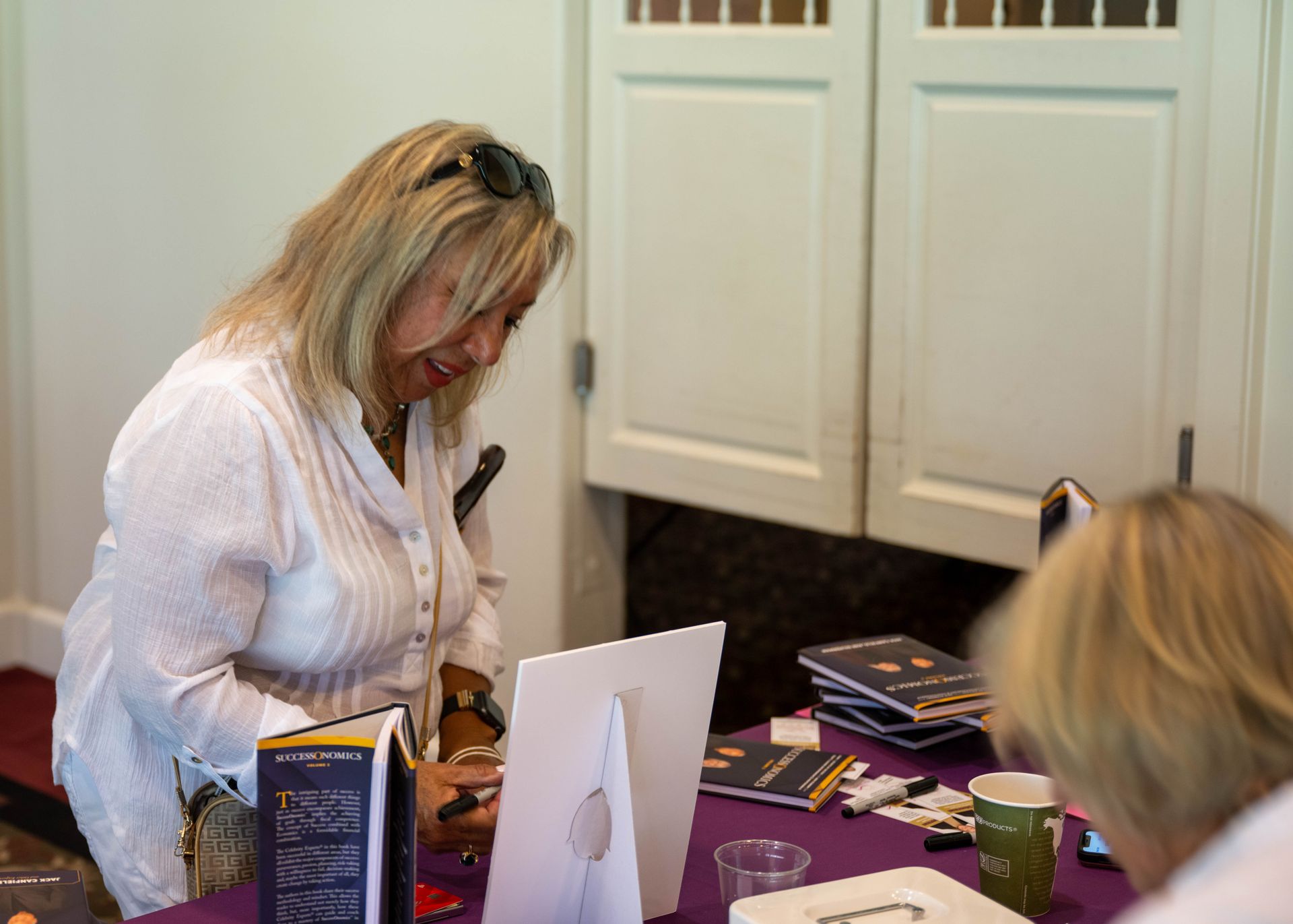 A woman in a white shirt is sitting at a table working on a computer