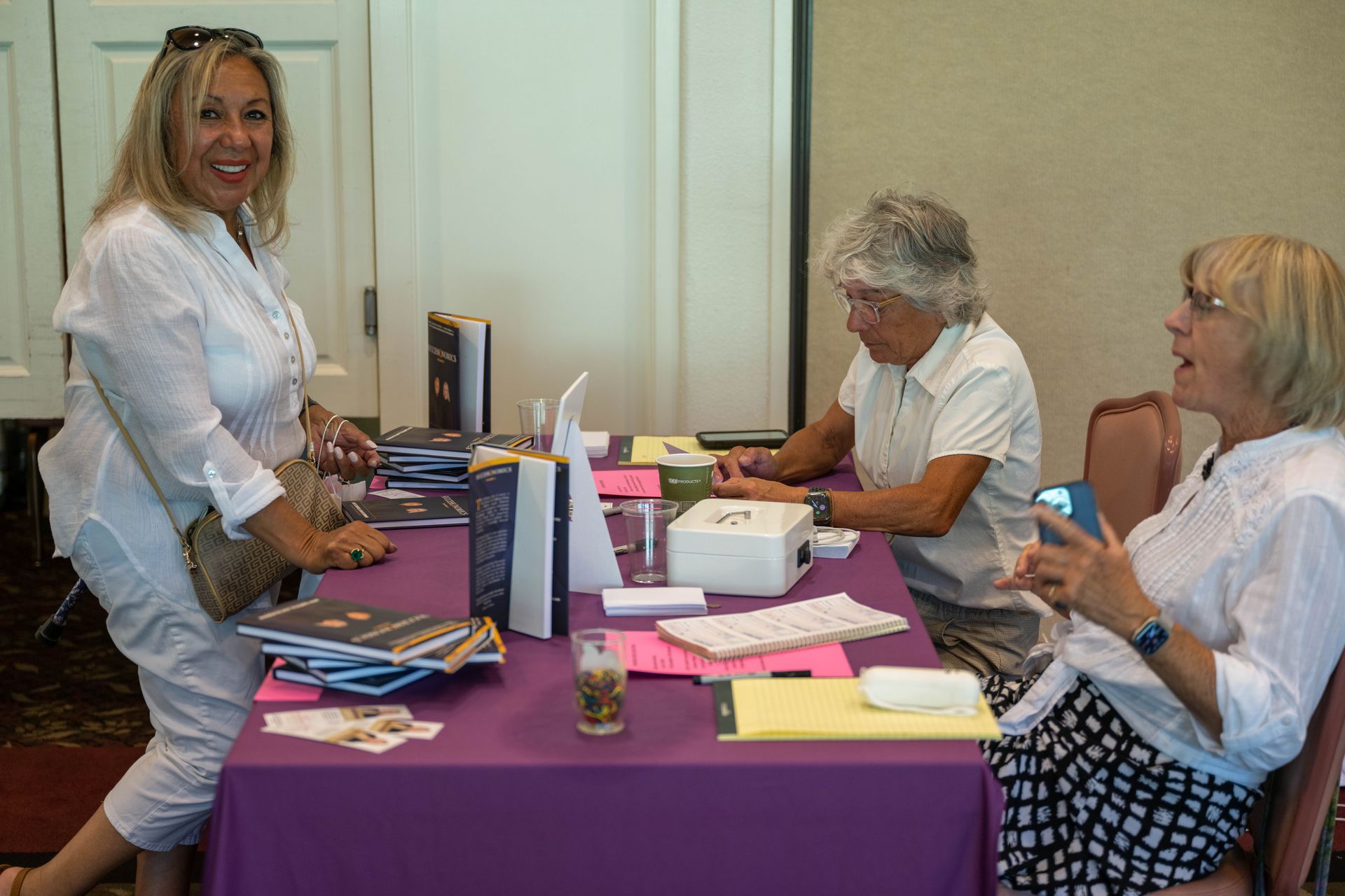 Three women are sitting at a table with a purple table cloth.