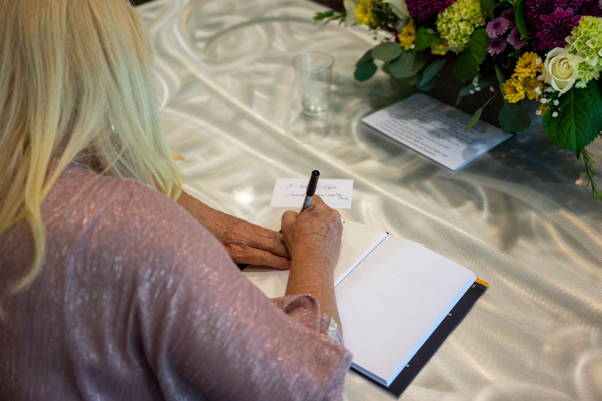 Kim Silverman is sitting at a table autographing her SuccessOnomics book.