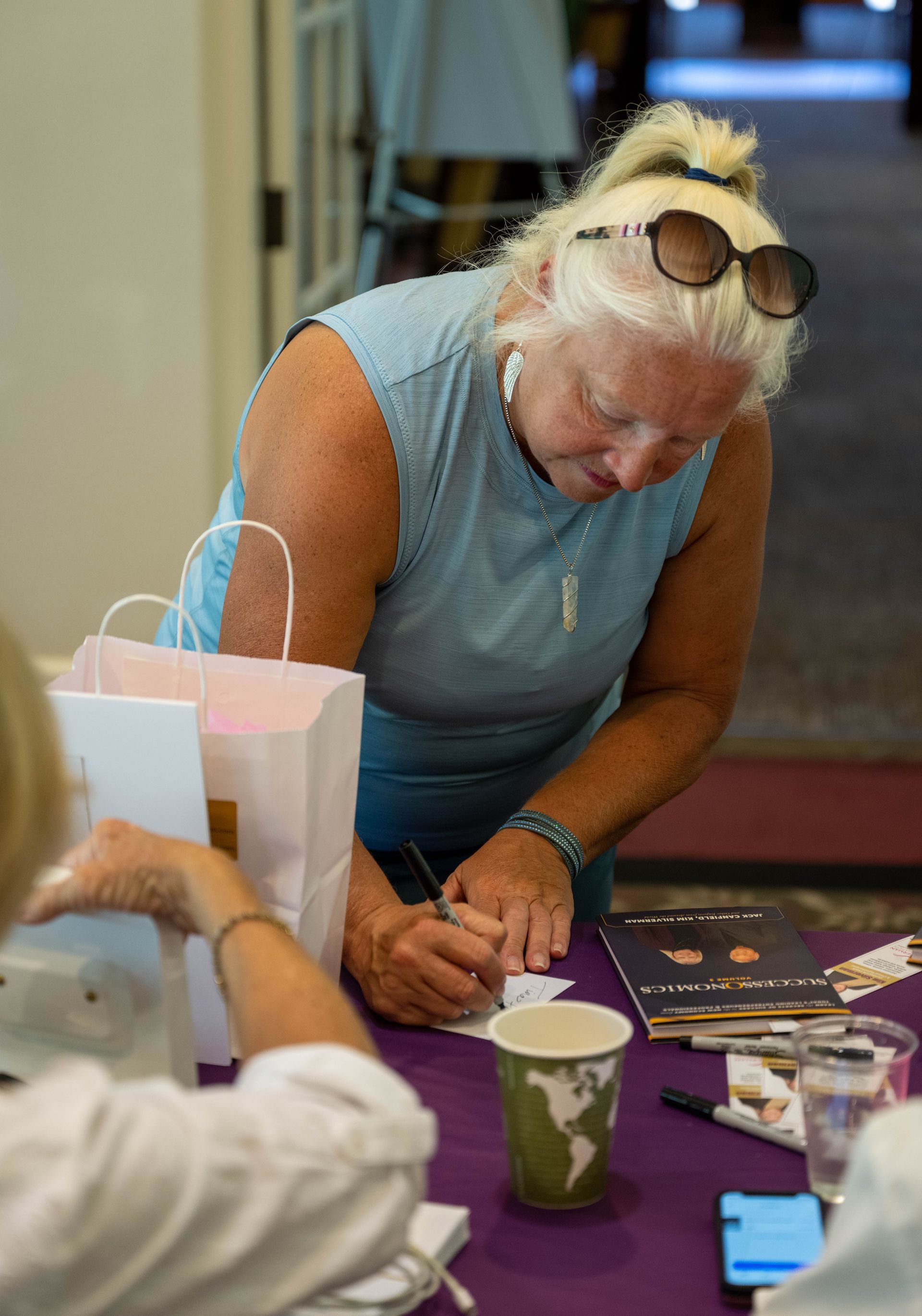 A woman is sitting at a table writing on a piece of paper.