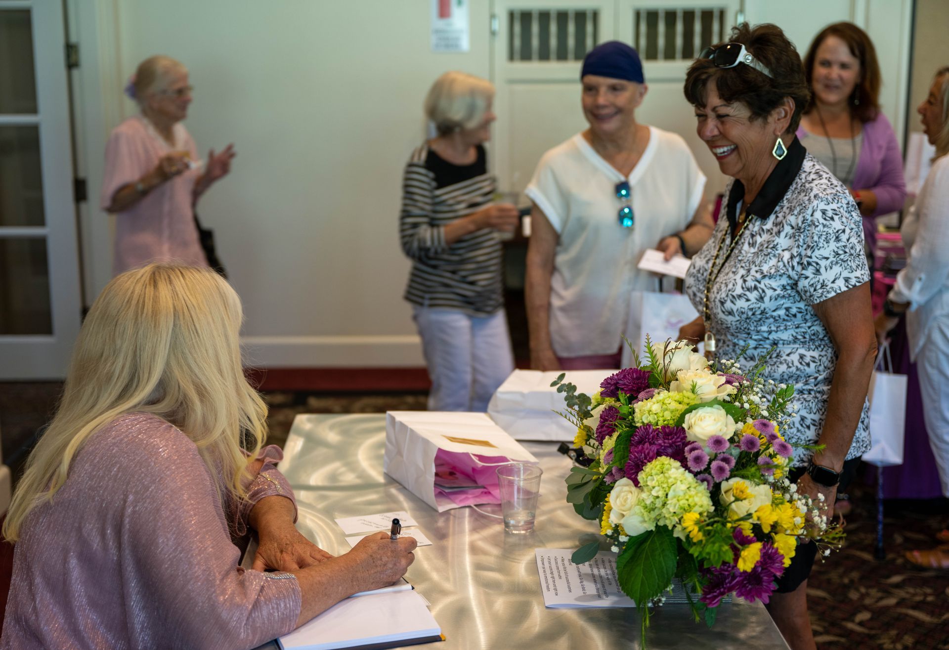 A group of women are standing around a table with flowers.