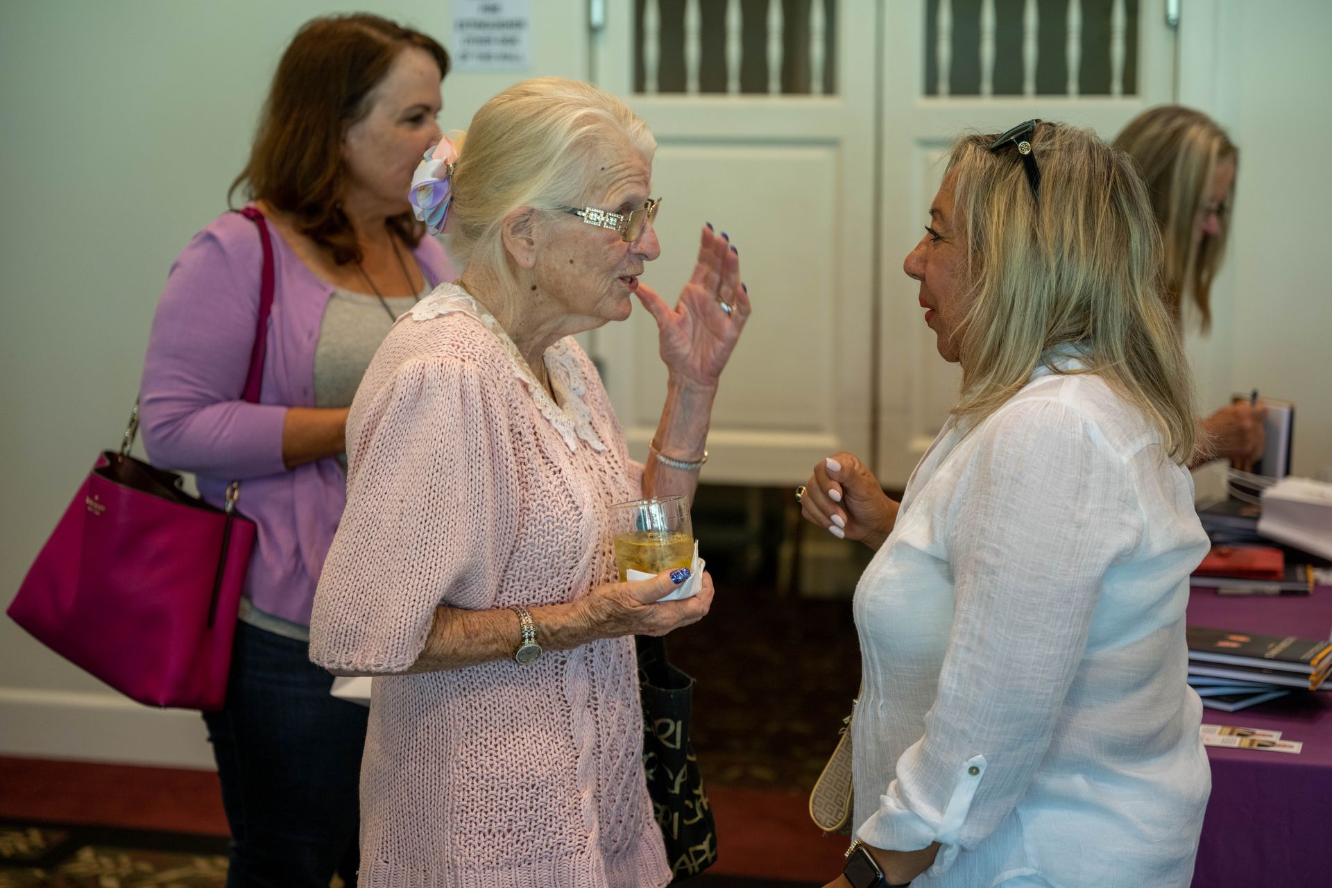 A group of women are standing around a table talking to each other.