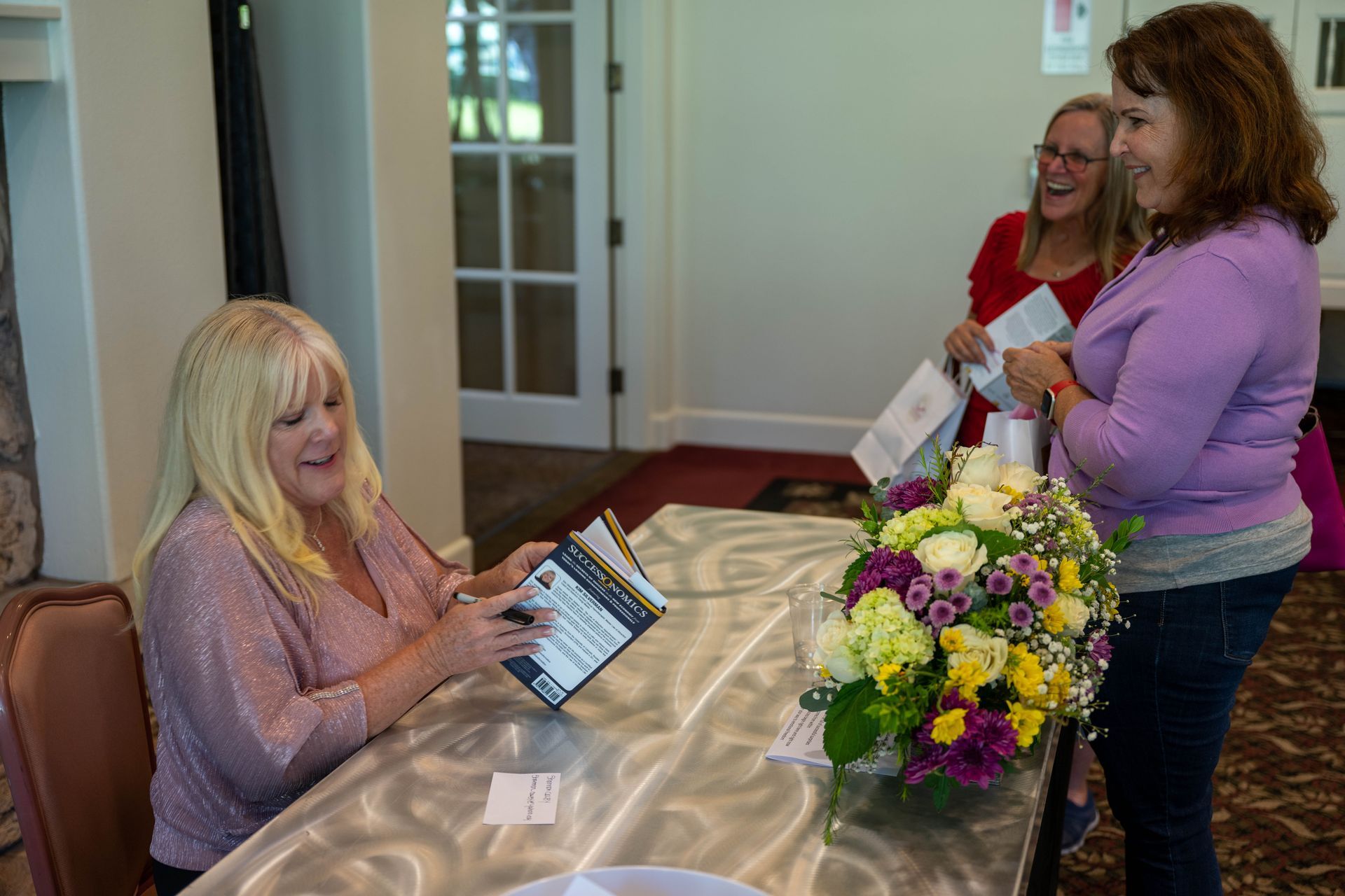 Kim Silverman is sitting at a table with a vase of flowers and a book.