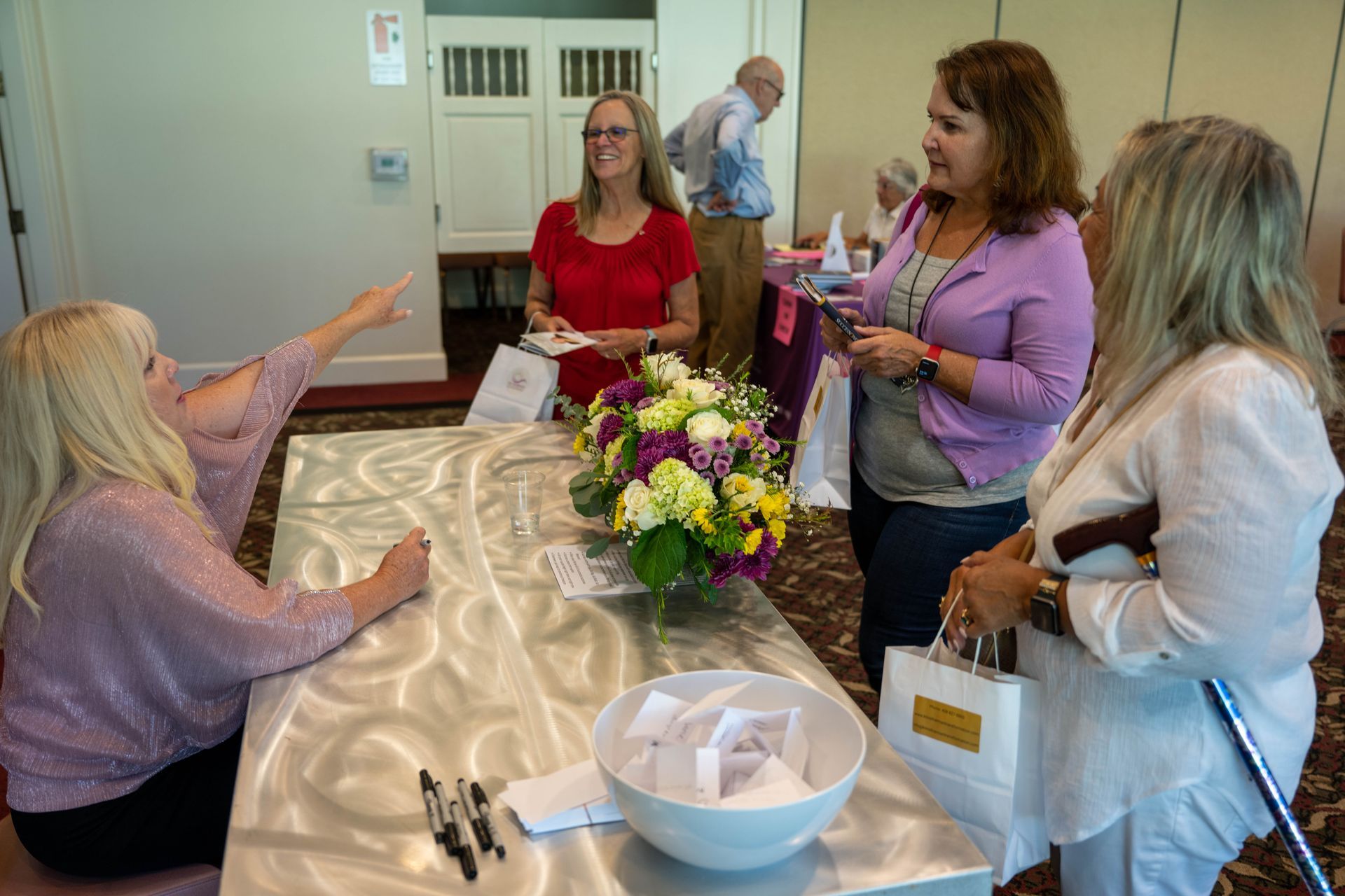 A group of women are standing around a table with flowers on it.