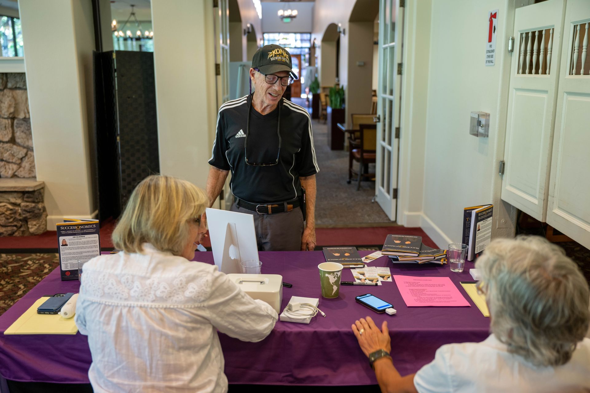 A man is standing next to a woman sitting at a table.