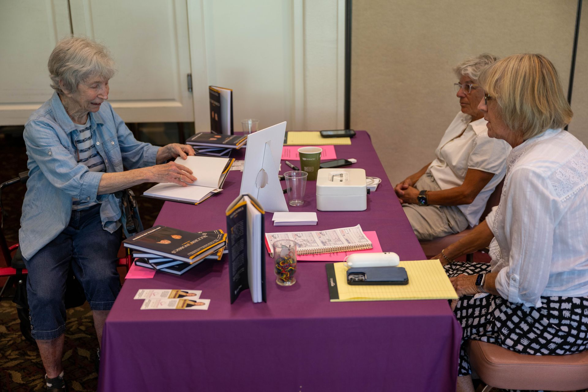 Three women are sitting at a table with a purple table cloth.