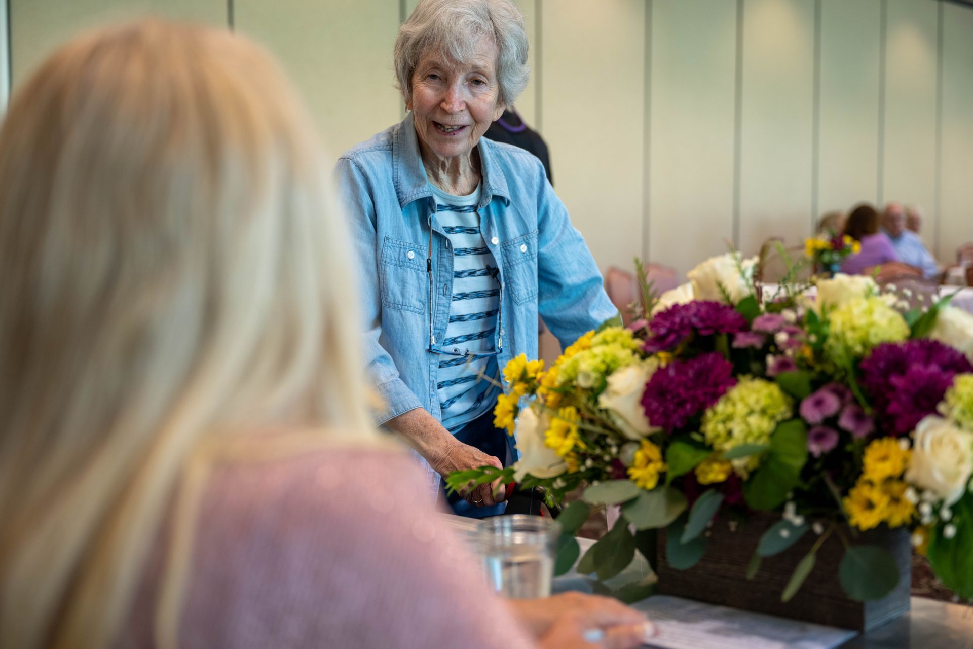 A woman is sitting at a table with a vase of flowers in front of her.