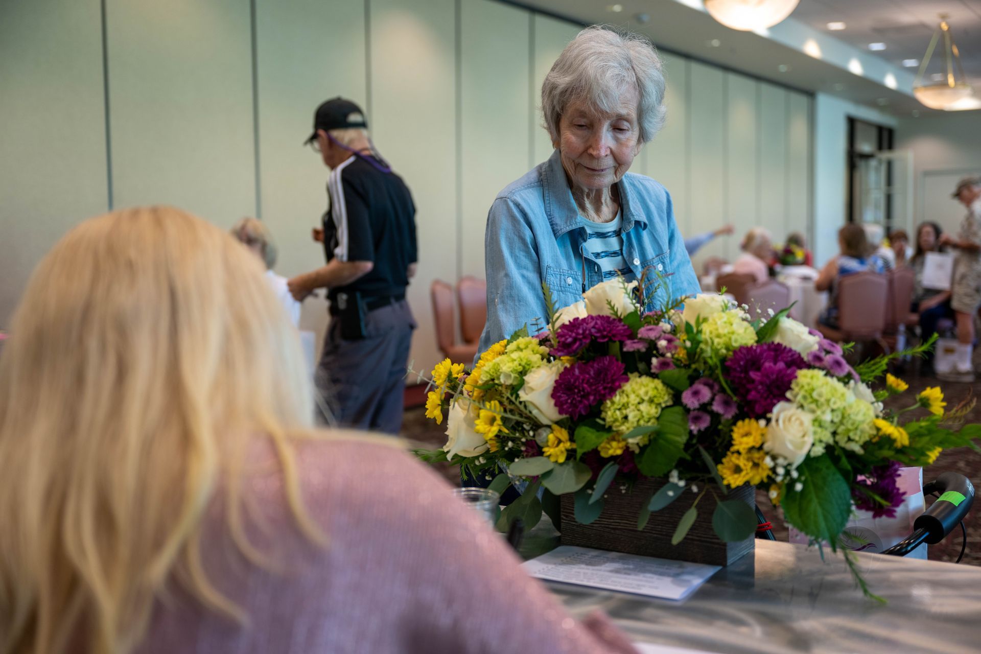 A woman is sitting at a table with a vase of flowers in front of her.