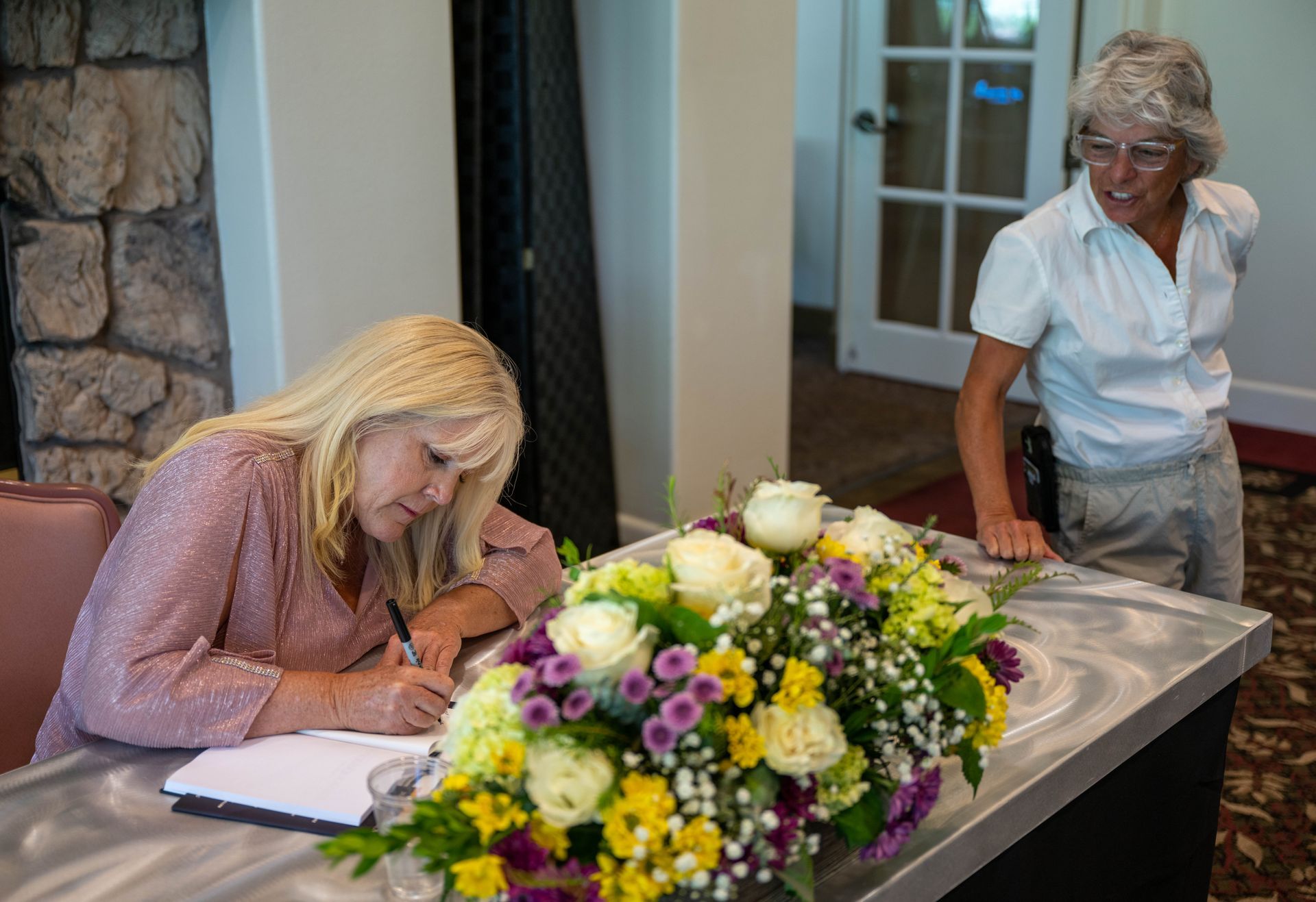 Kim Silverman sitting at a table with flowers in front of them signing SuccessOnomics book.